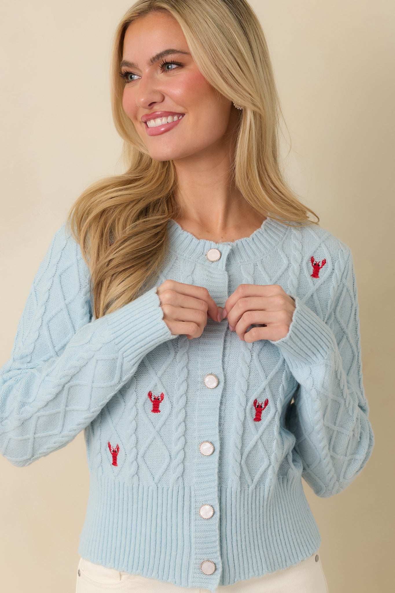 Light blue cardigan styled buttoned, displaying embroidered lobster pattern and ribbed hem.
