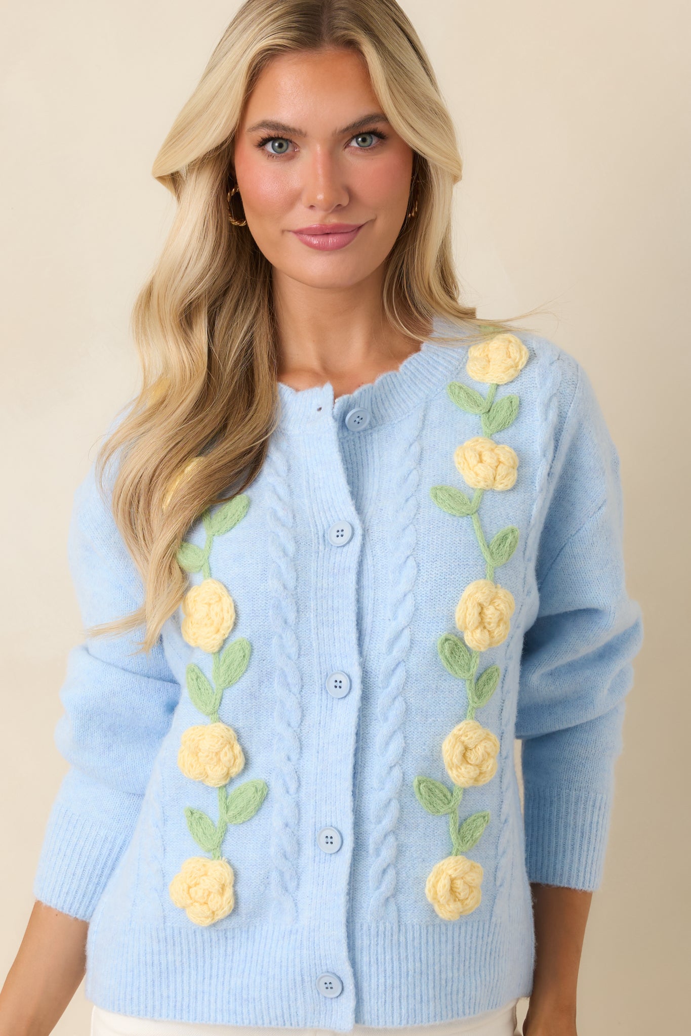 Blue knit cardigan highlighting the button-front closure, floral accents, and textured stitching details.