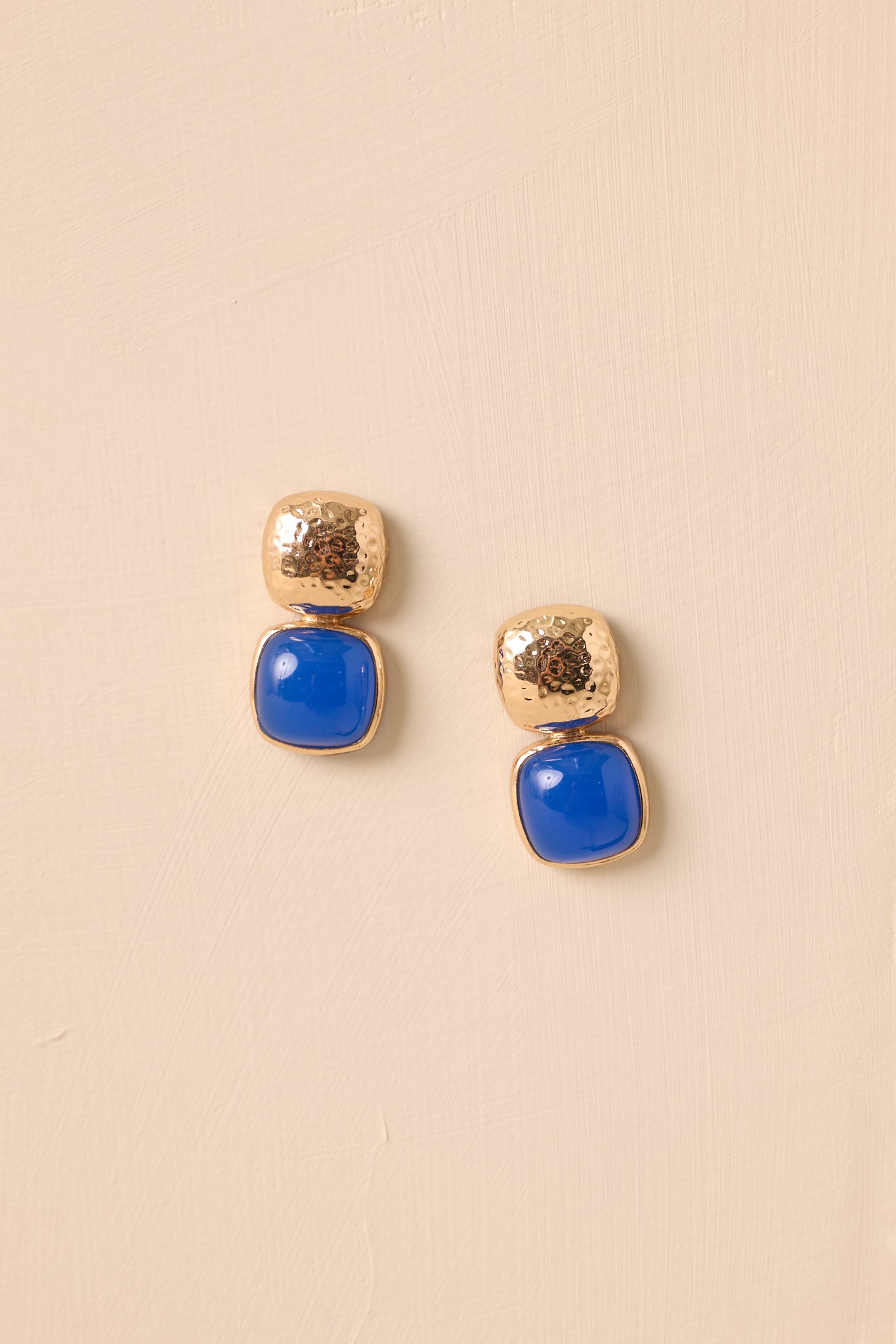 These blue earrings feature a gold textured square stud, a blue stone square drop design, and secure post backings.