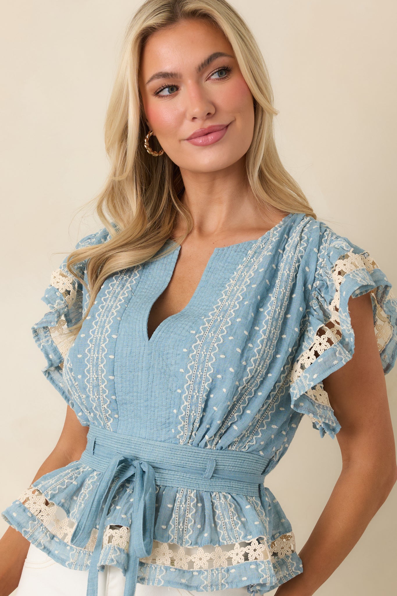 Close-up of blue fabric with beige floral embroidered lace and finely stitched peplum hem.