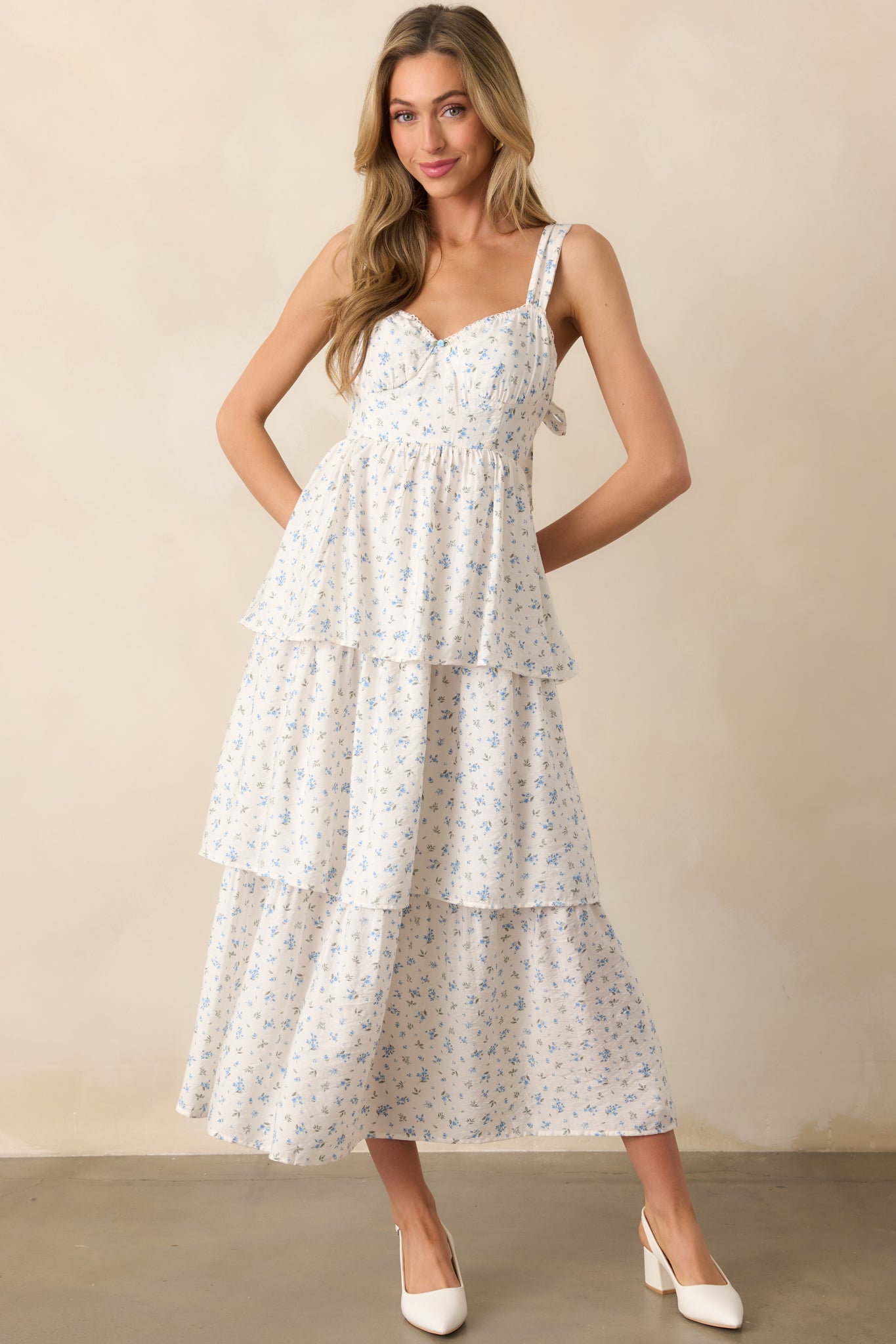 The blue floral maxi dress shown from the front, featuring the tiered skirt, adjustable straps, and bustier-style bodice with stitch detailing. The elastic sweetheart neckline and small center bust flower add a feminine touch.