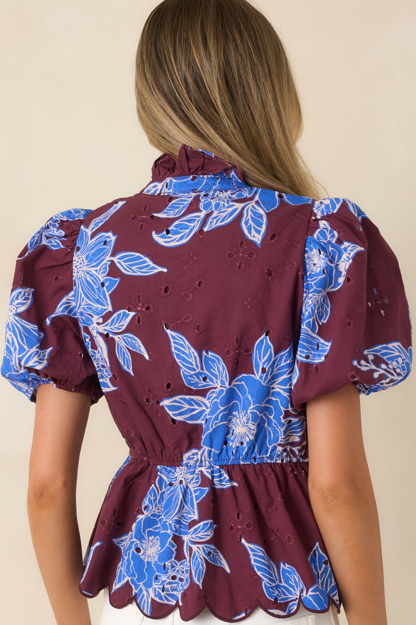 Rear view of the blue floral top featuring an elasticized waist, puff sleeves, and scalloped hem.