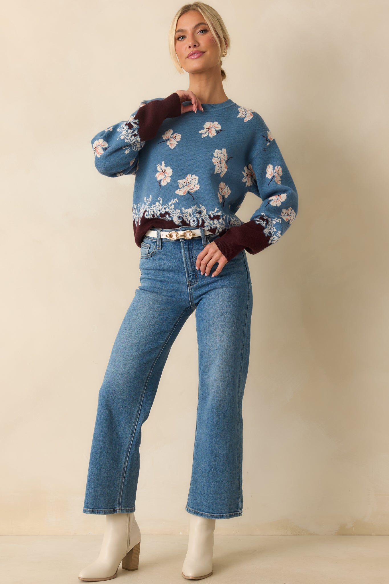 Blue knit sweater showcasing ivory floral motifs and a decorative brown hemline.