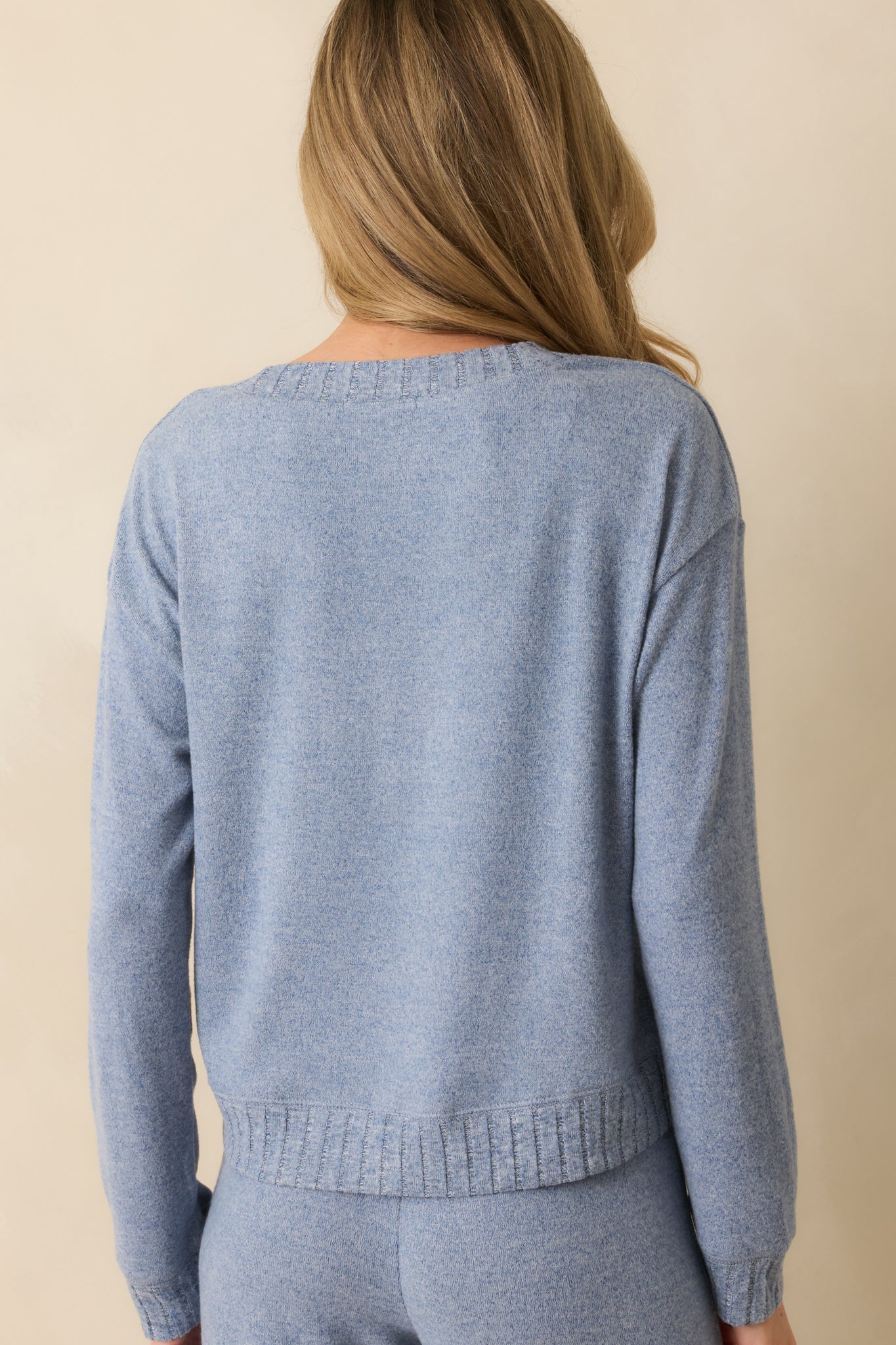 Rear view of blue knit sweater showing relaxed fit, long sleeves, and ribbed hem without any embellishments.