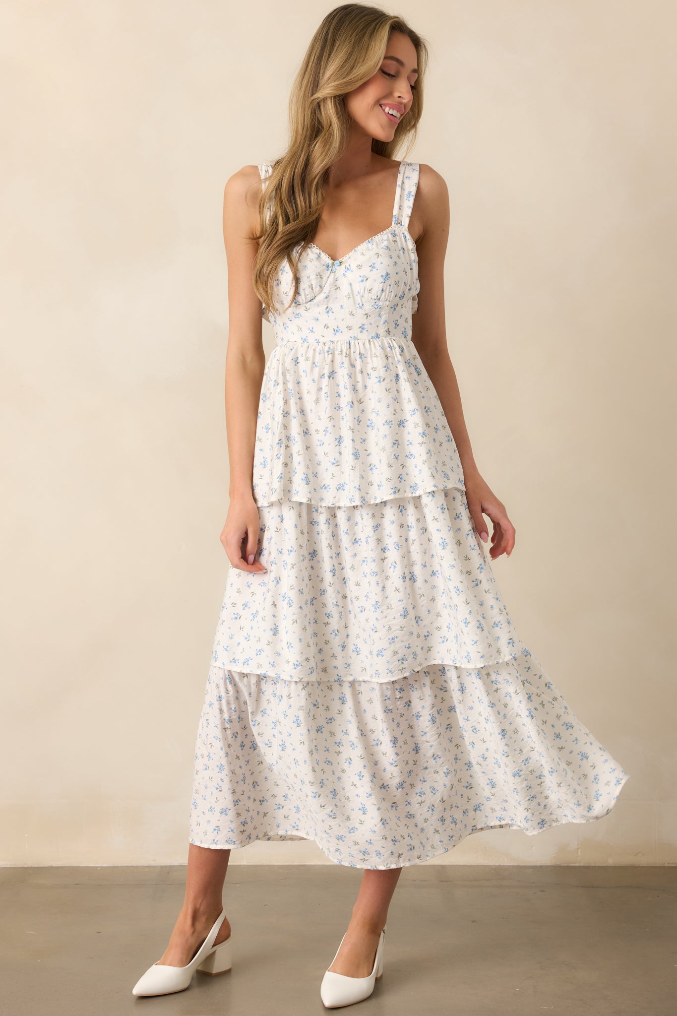 A full-body front view of a blue floral maxi dress, featuring an elastic sweetheart neckline, adjustable straps, and bustier-style stitch detailing in the bodice. The tiered skirt and smocked back panel add flow and movement to the dress.