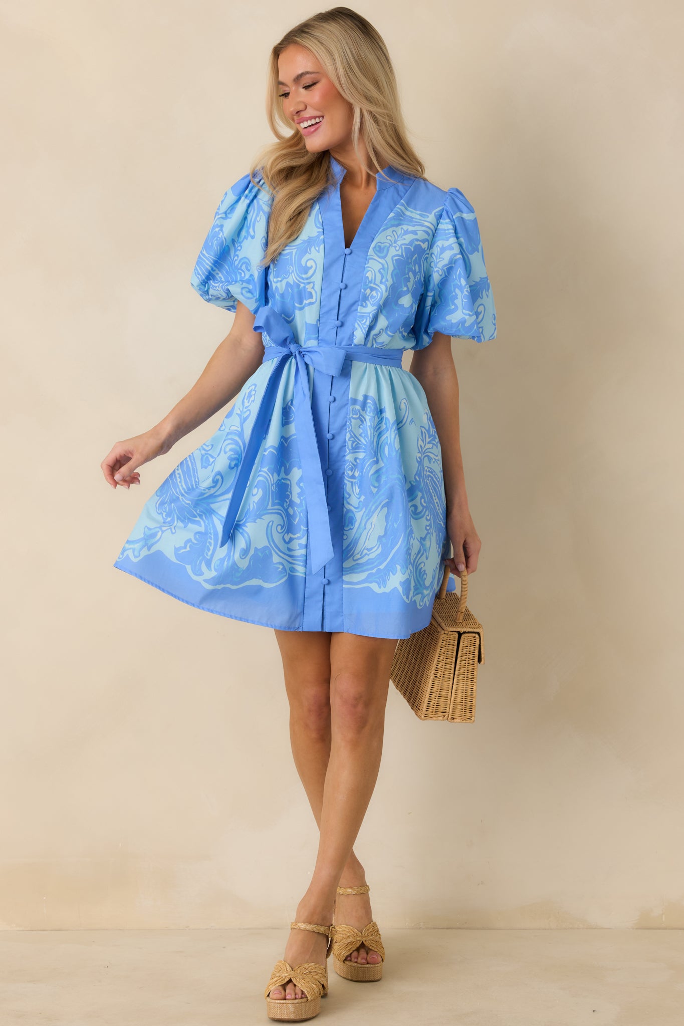 Blue paisley mini dress with a V-neckline, functional button-front closure, and short puff sleeves in lightweight woven cotton.