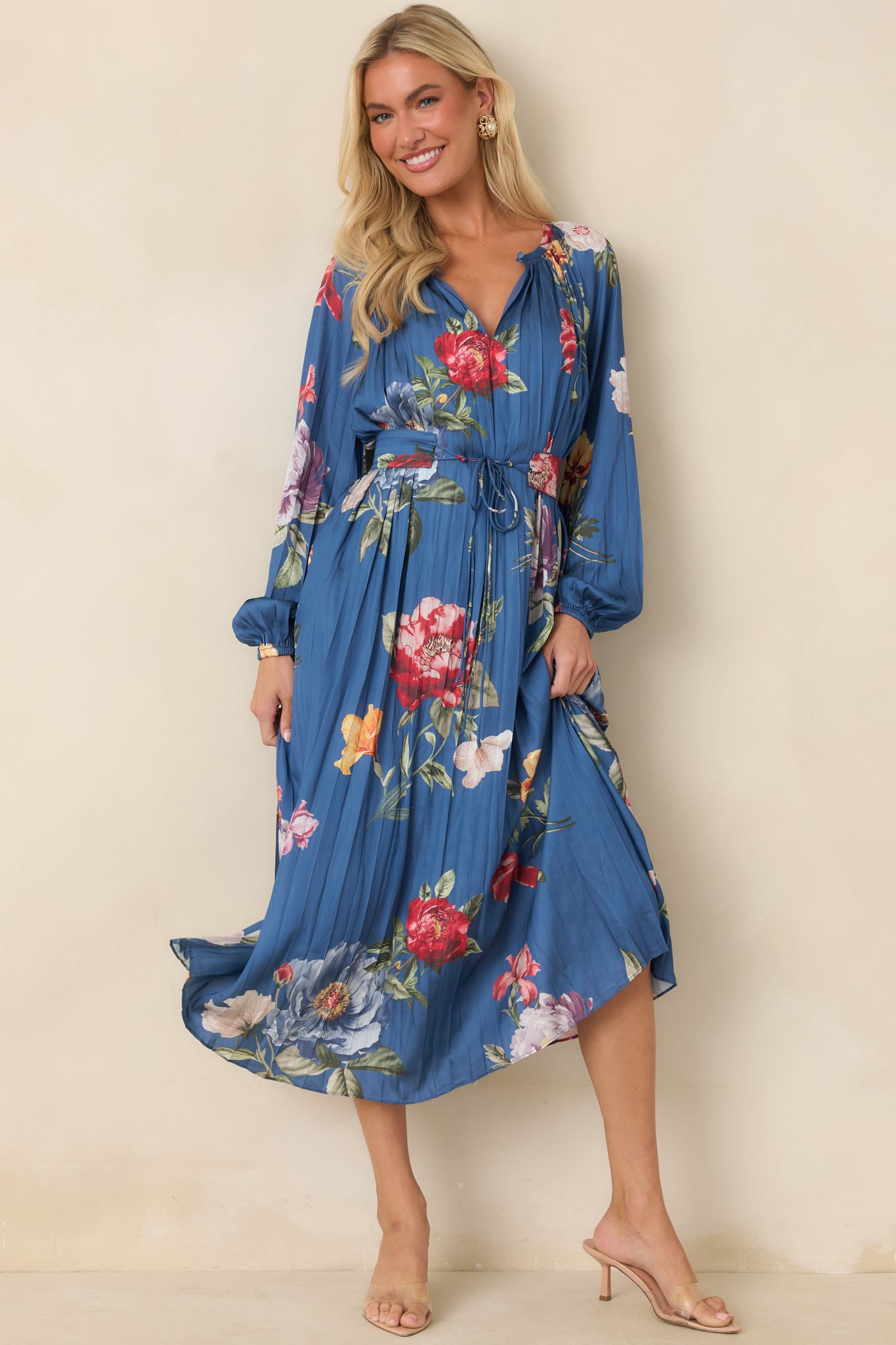 Blue pleated midi dress featuring oversized multicolor floral prints, a gathered split neckline, and a flowing silhouette.