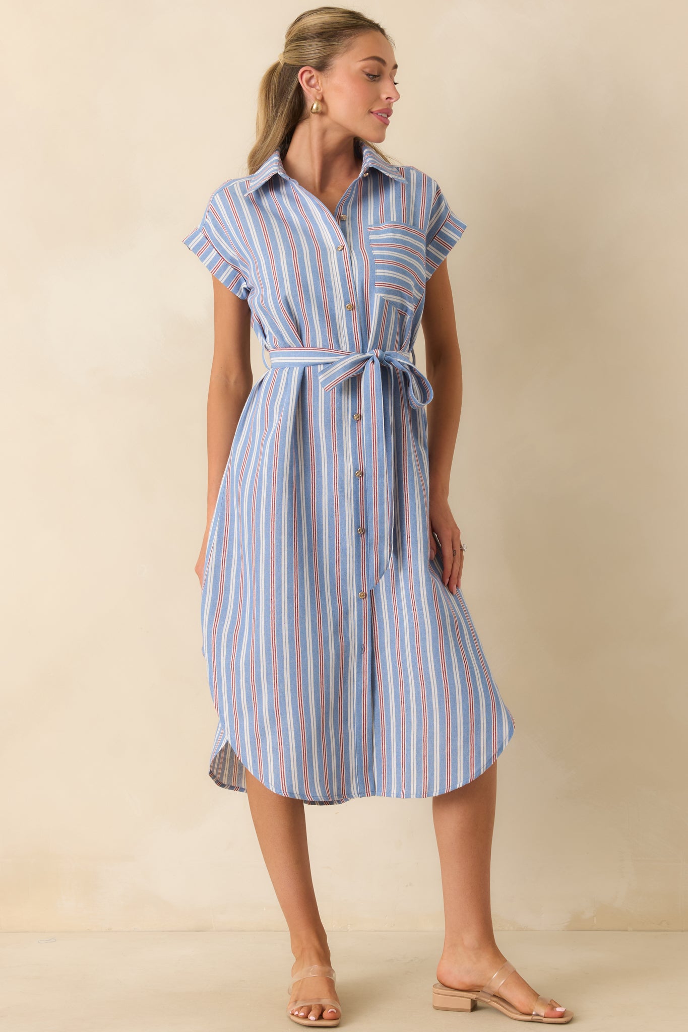 Blue, red, and ivory striped midi dress designed with a relaxed button-front silhouette, cap sleeves, and a curved shirttail hem.