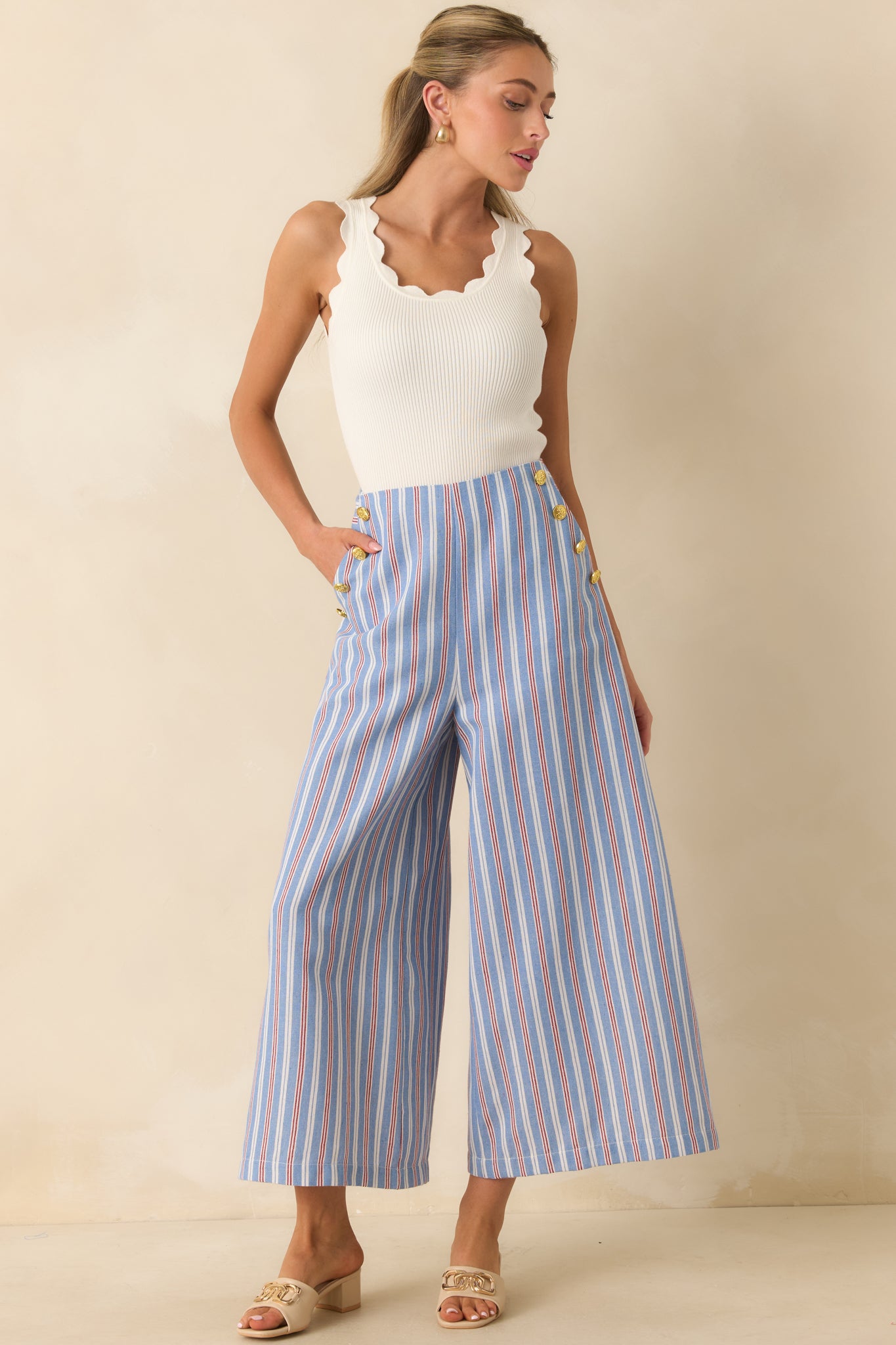 Cropped wide leg pants with a blue, red, and ivory stripe pattern, fitted high-rise waist, and polished gold-tone button accents.