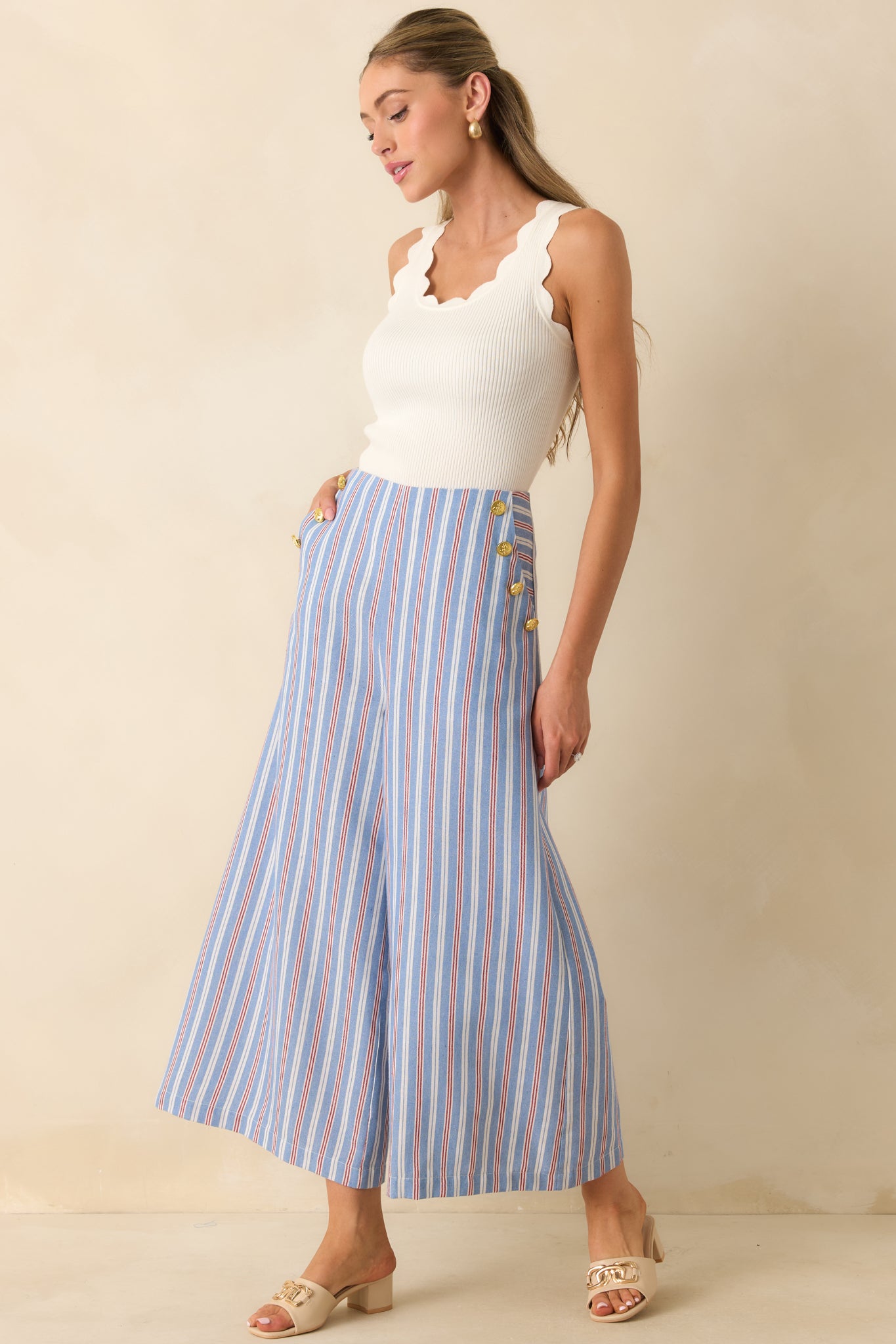 Blue, red, and ivory striped high-rise pants featuring a wide leg silhouette, cropped length, and decorative gold-tone sailor buttons at the hips.
