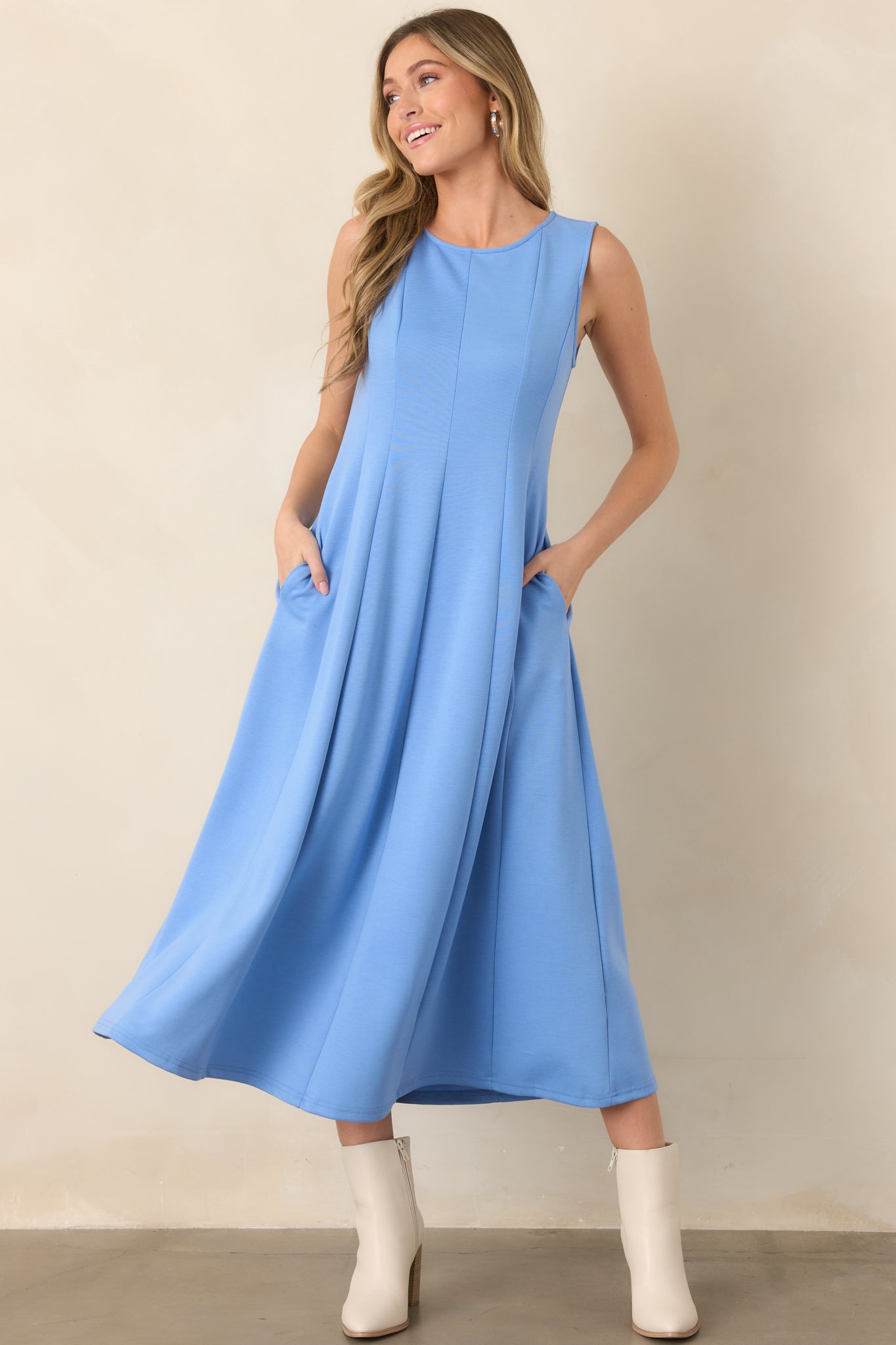 Blue sleeveless dress displaying a streamlined bodice, round neckline, hidden side pockets, and softly flared midi-length skirt.