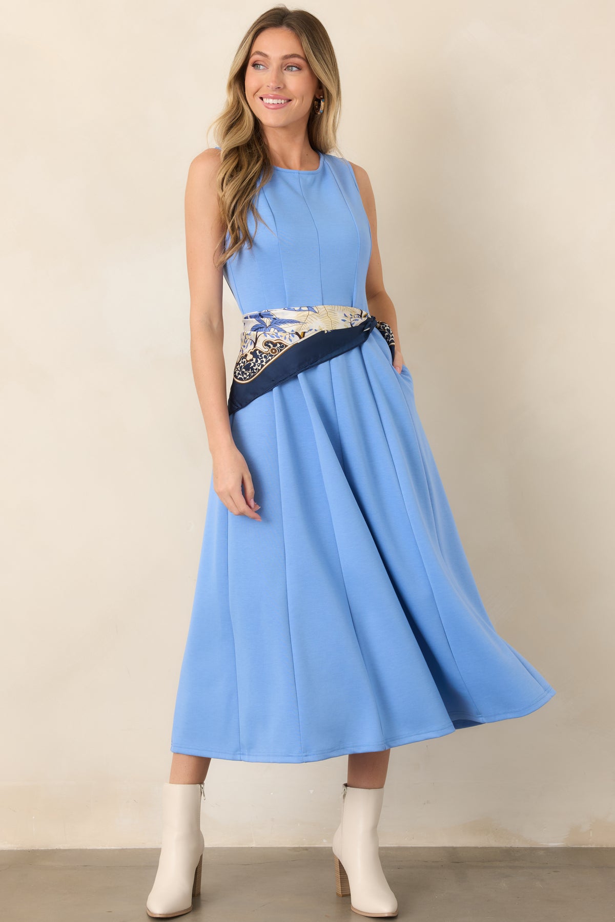 Blue midi dress featuring a classic round neckline, sleeveless design, seamed panel construction, and flowing silhouette.