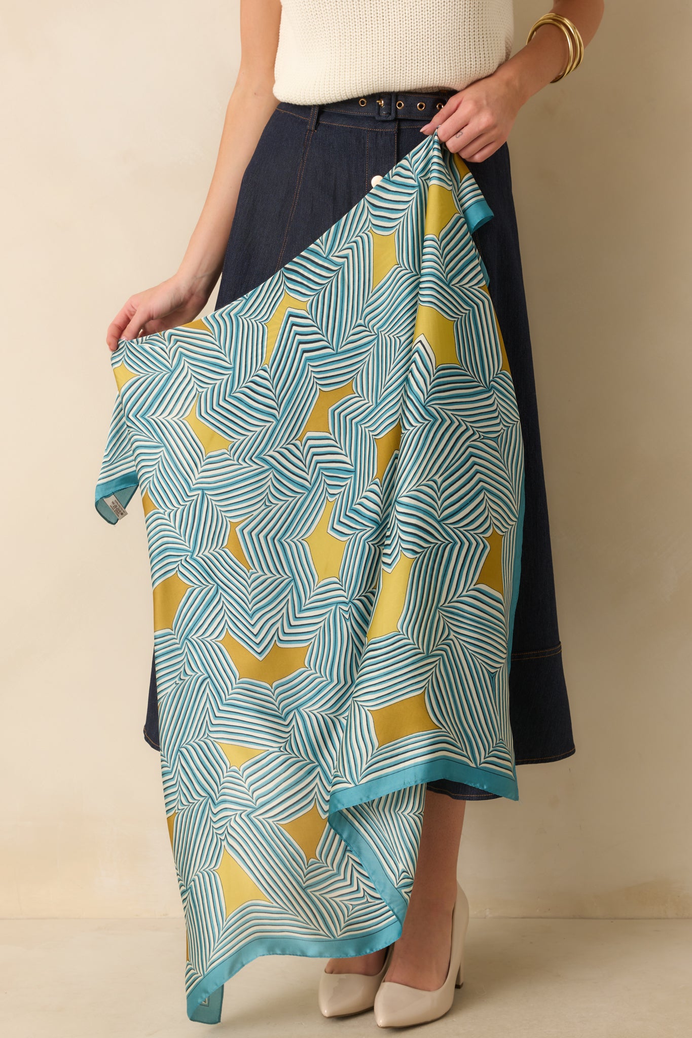 A full view of the blue square scarf with a geometric stripe pattern and golden yellow accents, showing a smooth satin finish.