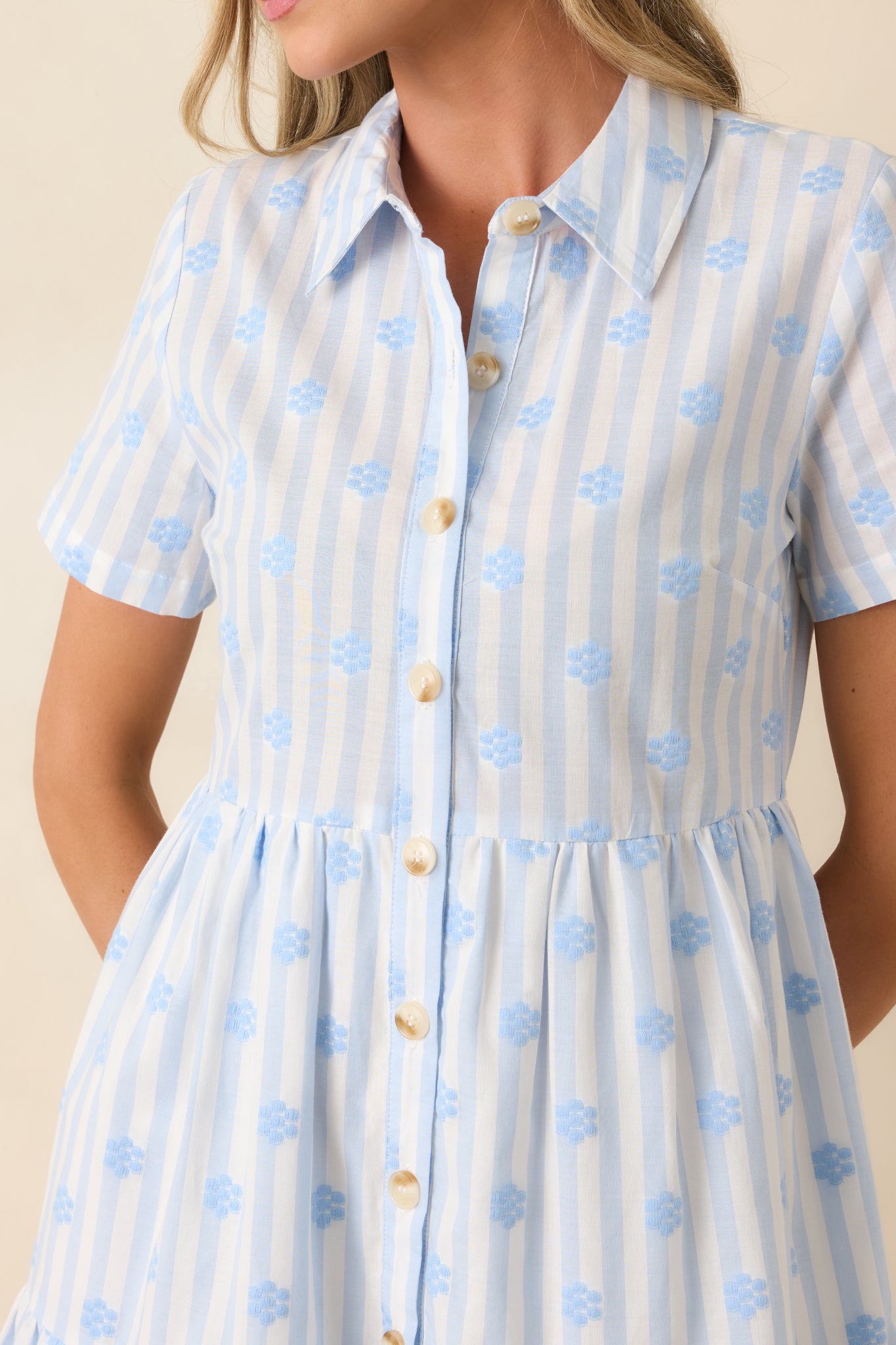 Close-up of blue stripe cotton mini dress featuring embroidered floral accents, button front detailing, and fabric texture.