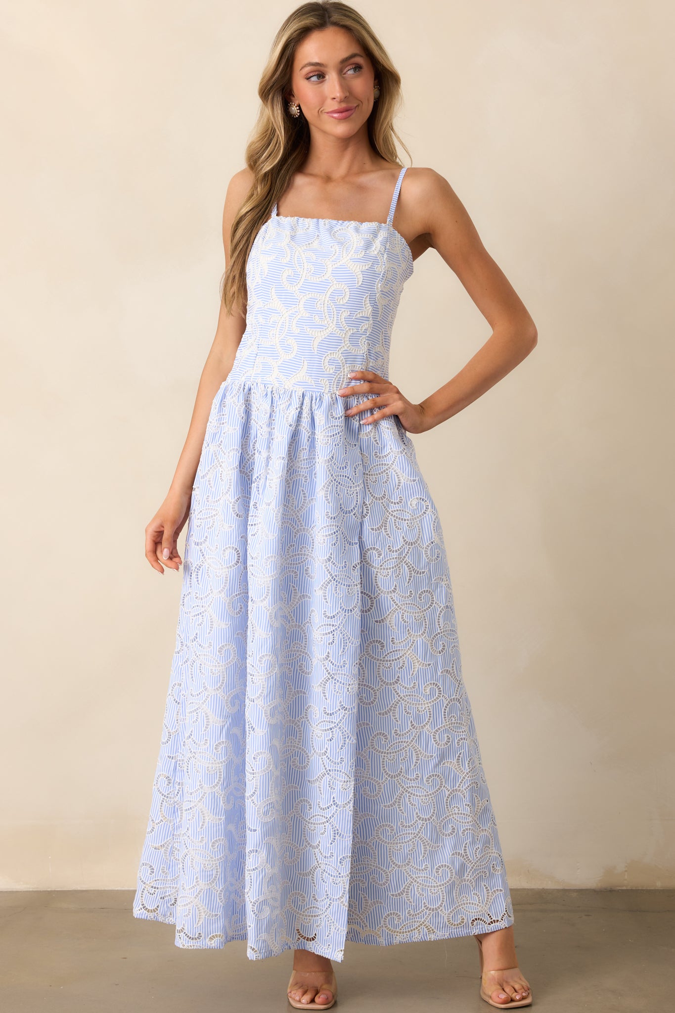 A flowing maxi dress with a blue stripe pattern overlay and delicate eyelet embroidery. The square neckline and hidden back zipper create a seamless, elegant look.