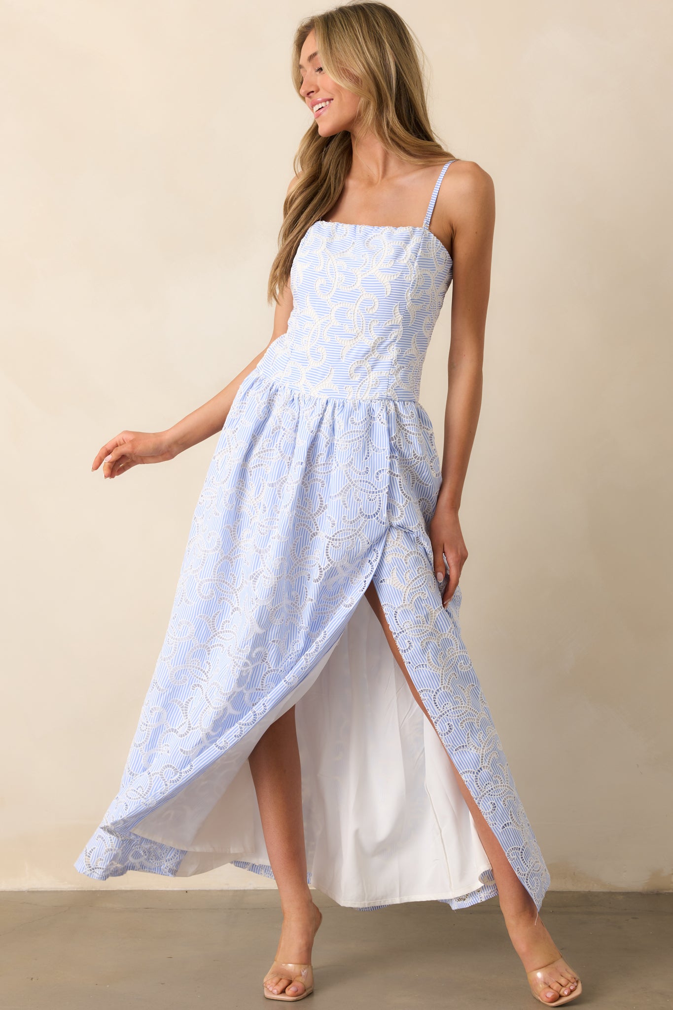 A maxi dress featuring blue and white stripes, intricate embroidered eyelets, and a smocked back panel. The optional adjustable straps and silicone non-slip grip strips ensure a secure fit.
