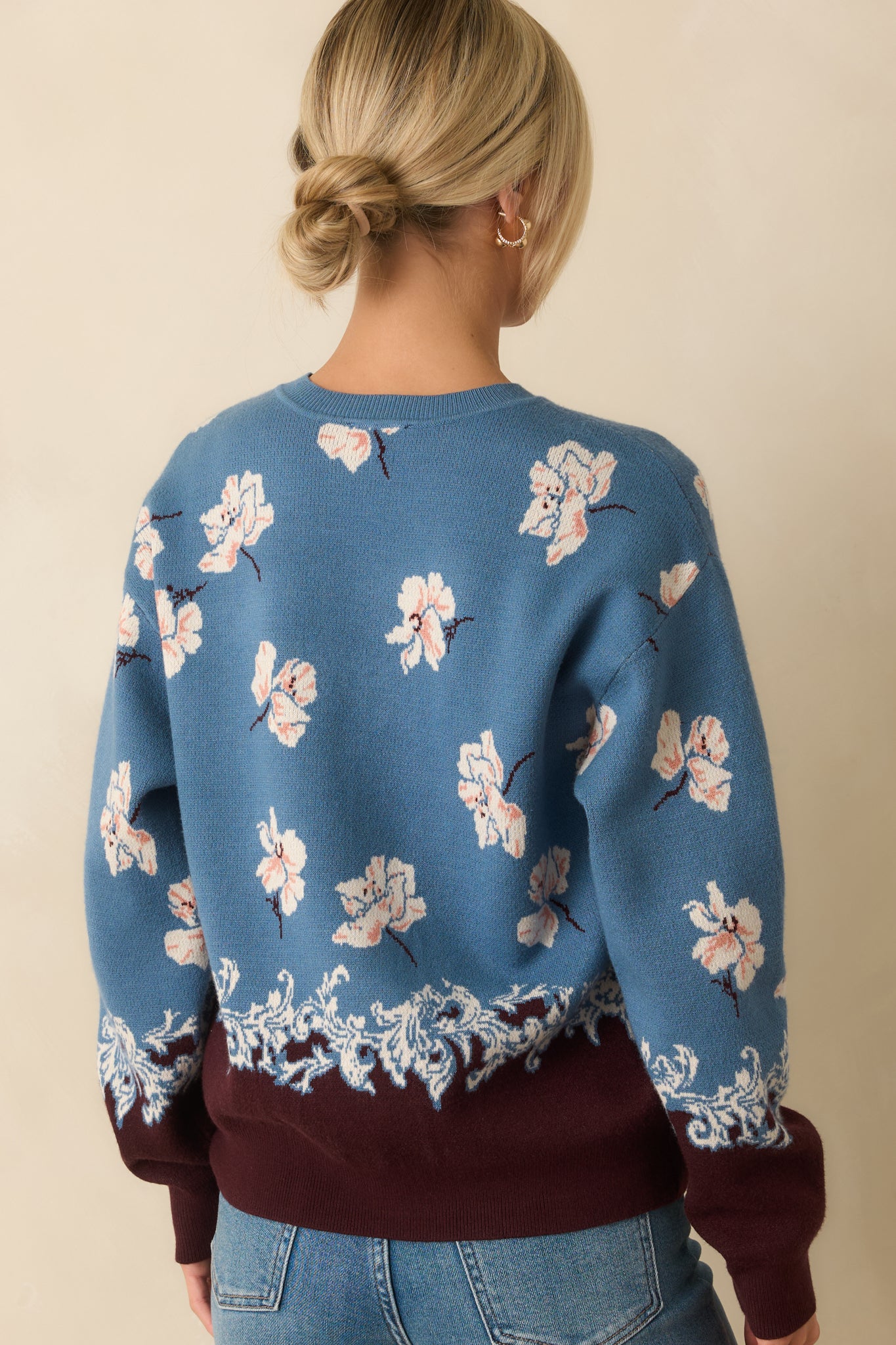 Rear view of the blue sweater featuring the ivory floral jacquard knit and brown contrast hem.