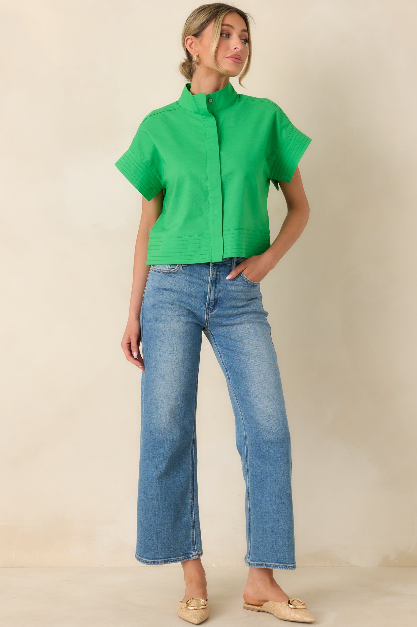 Boxy green top with smooth front closure, short cuffed sleeves, and streamlined mock neck design.