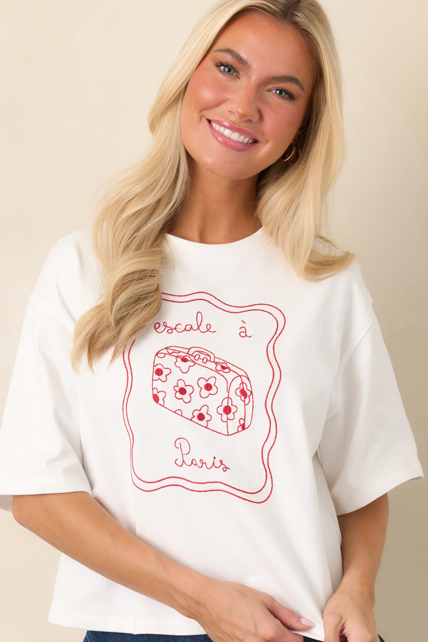 Detailed view of the relaxed boxy silhouette and colorful red embroidered artwork featuring a floral suitcase and Paris lettering.