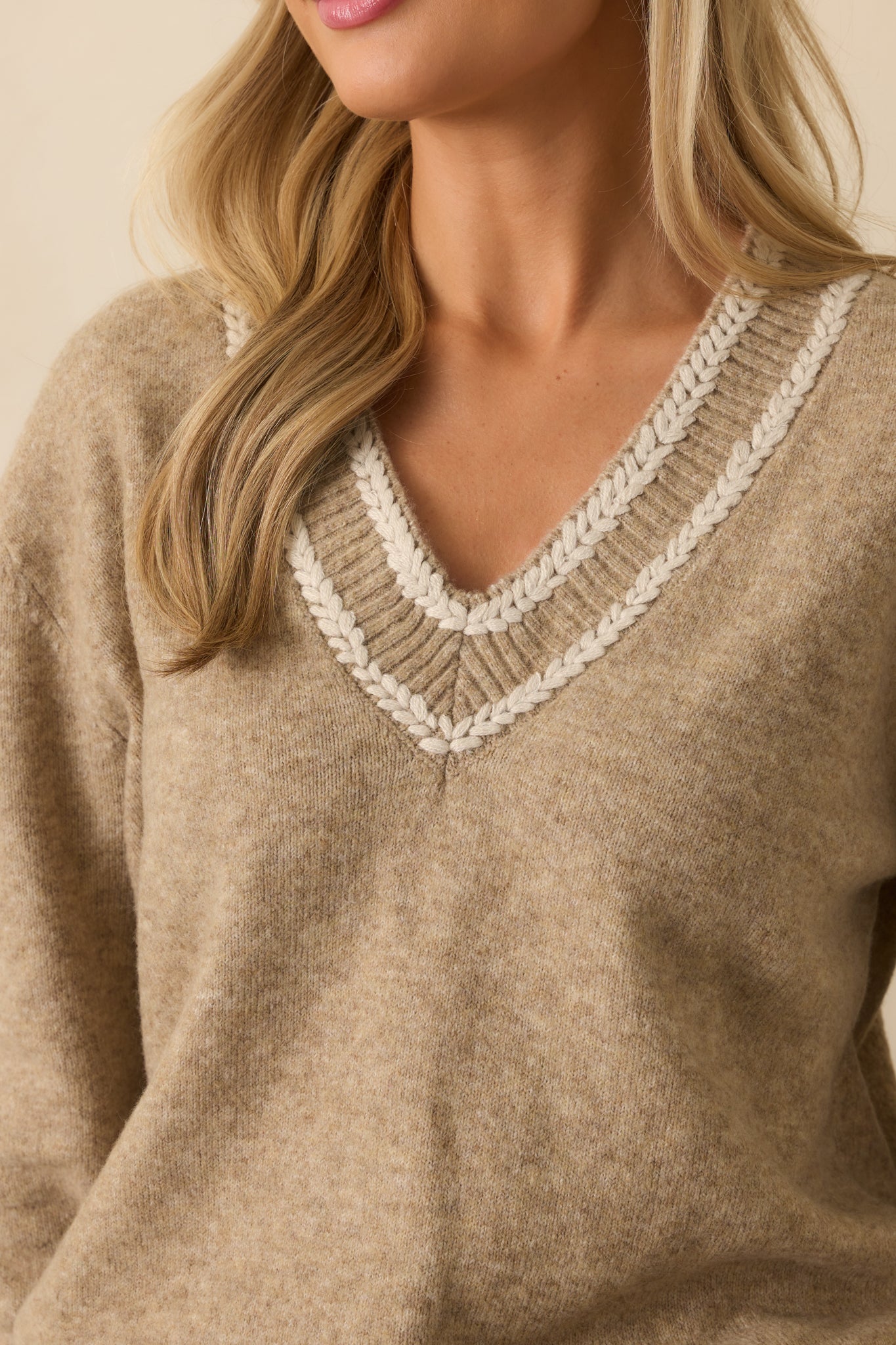 Braided ivory trim along the V-neckline of the tan knit sweater.