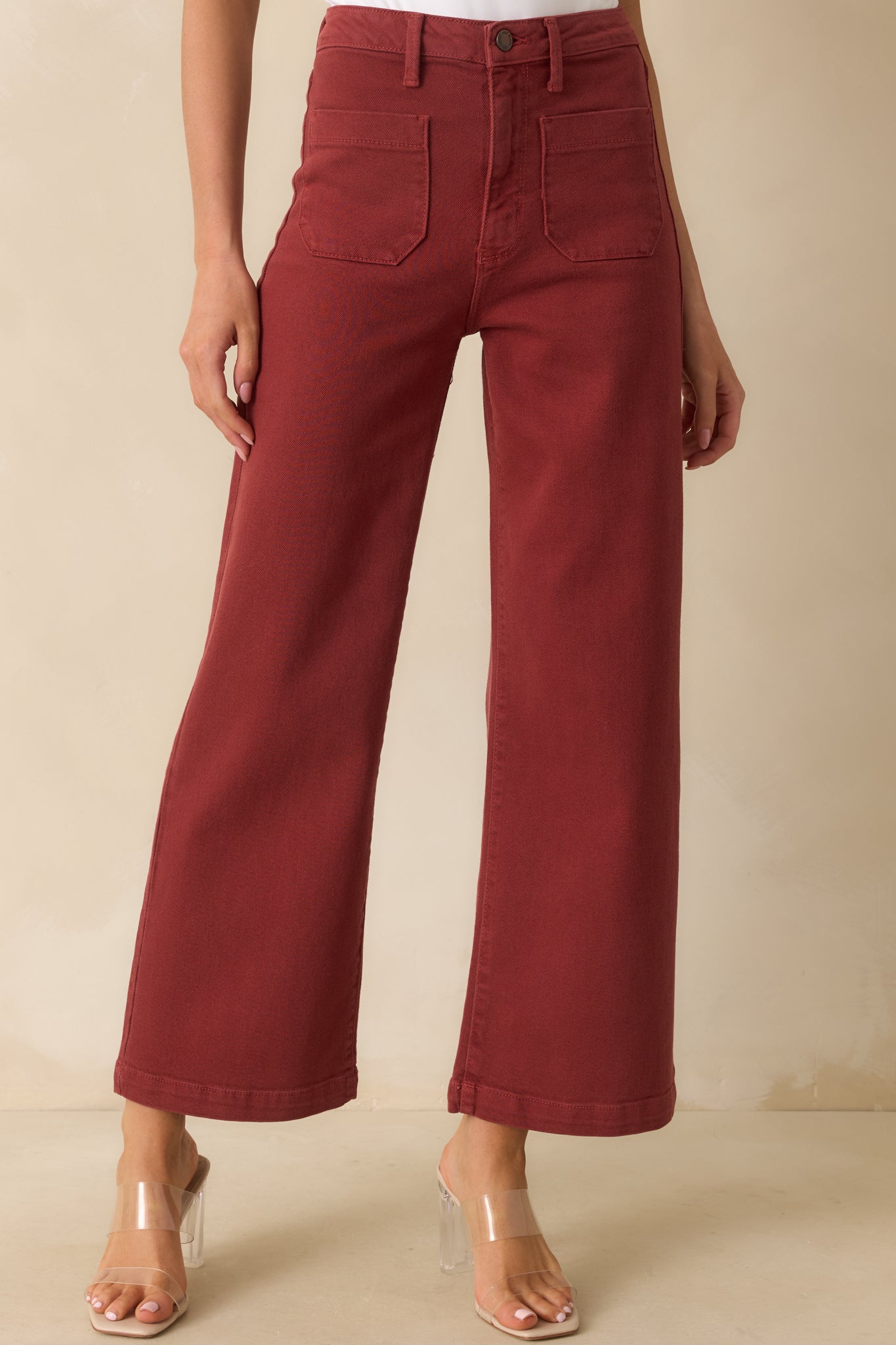 Close view of the high-rise waistband with button closure and belt loops on the brick red denim jeans.
