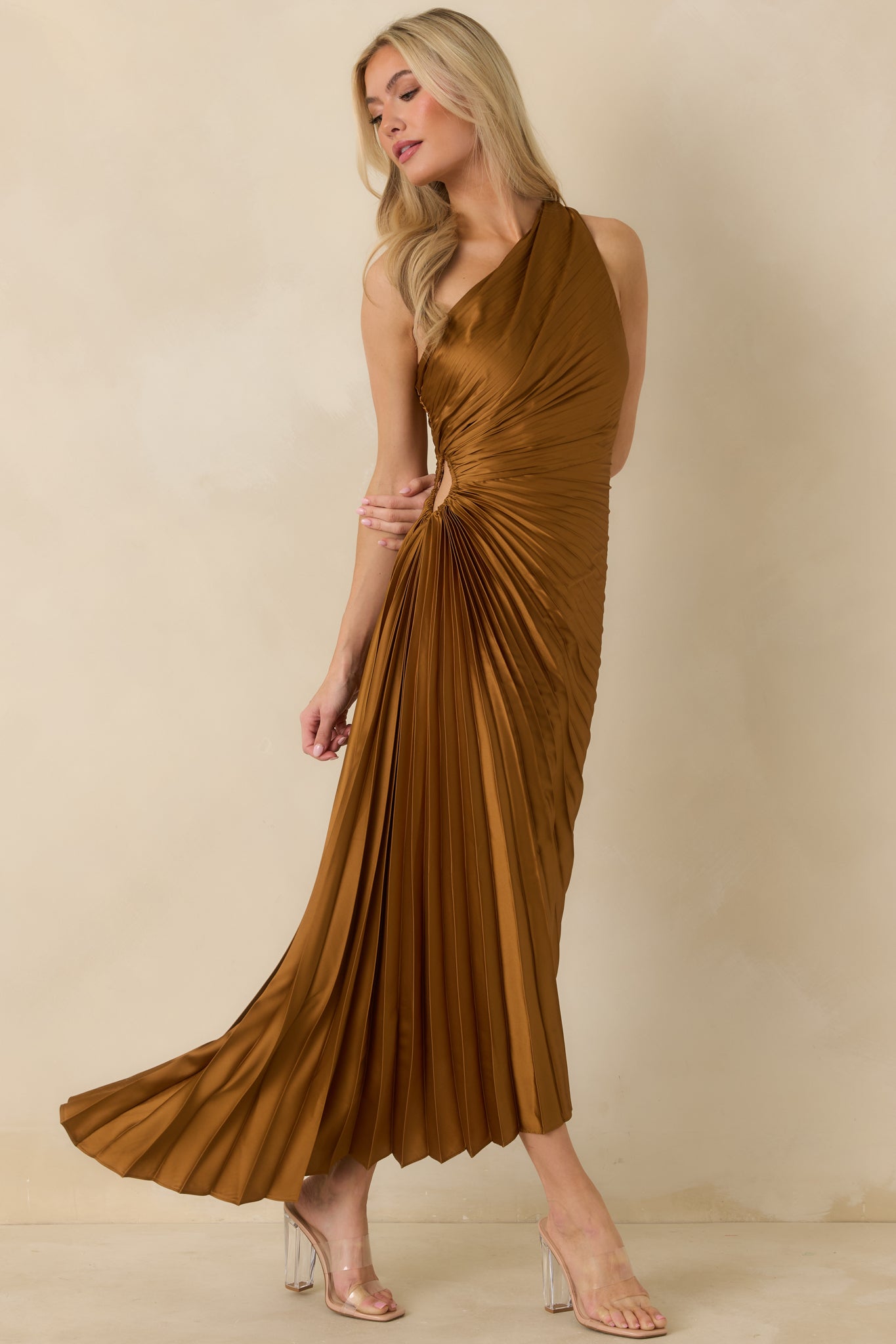 Front shot of bronze asymmetric maxi dress emphasizing pleated bodice, side cutout, and pleated skirt movement.