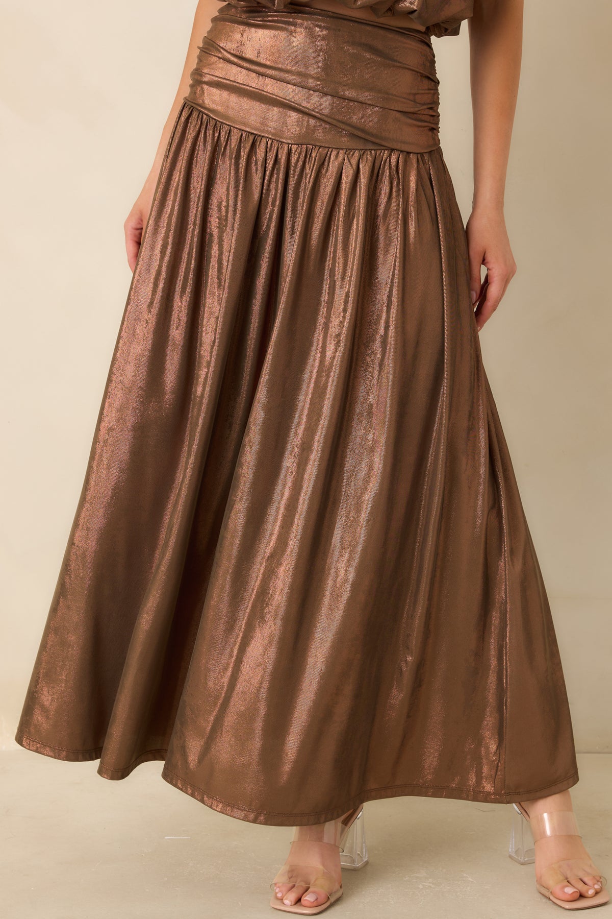 Gentle gathers beneath the bronze waistband create fullness through the flowing maxi skirt.