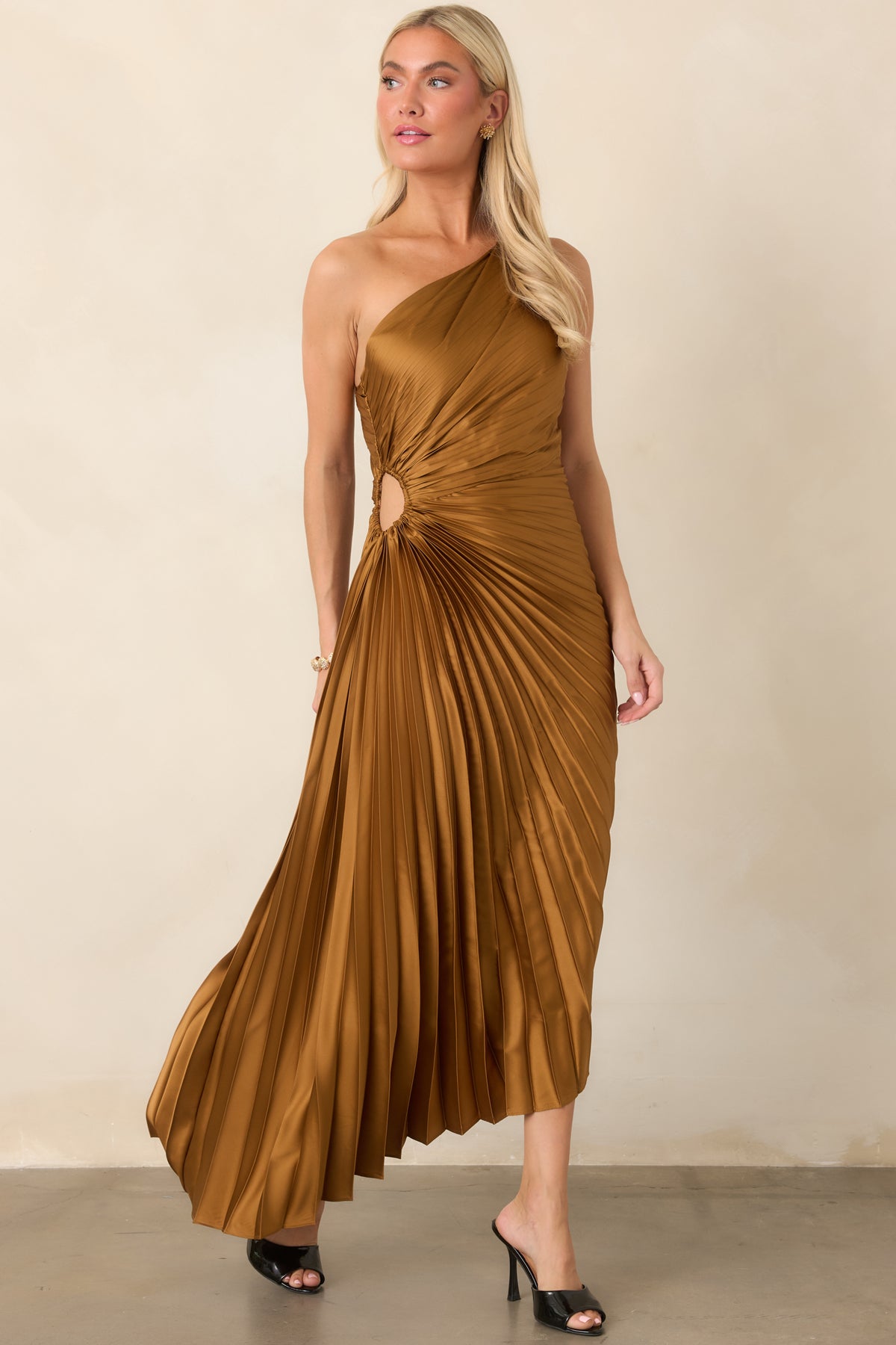 Metallic bronze maxi dress showcasing a sculpted one-shoulder neckline, finely pleated fabric, fitted waist, and fluid floor-length silhouette.