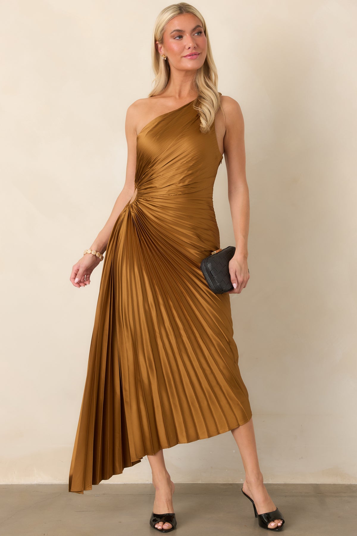 Shimmering bronze maxi dress with intricate pleated detailing throughout, a one-shoulder bodice, asymmetric hemline, and elongated silhouette.