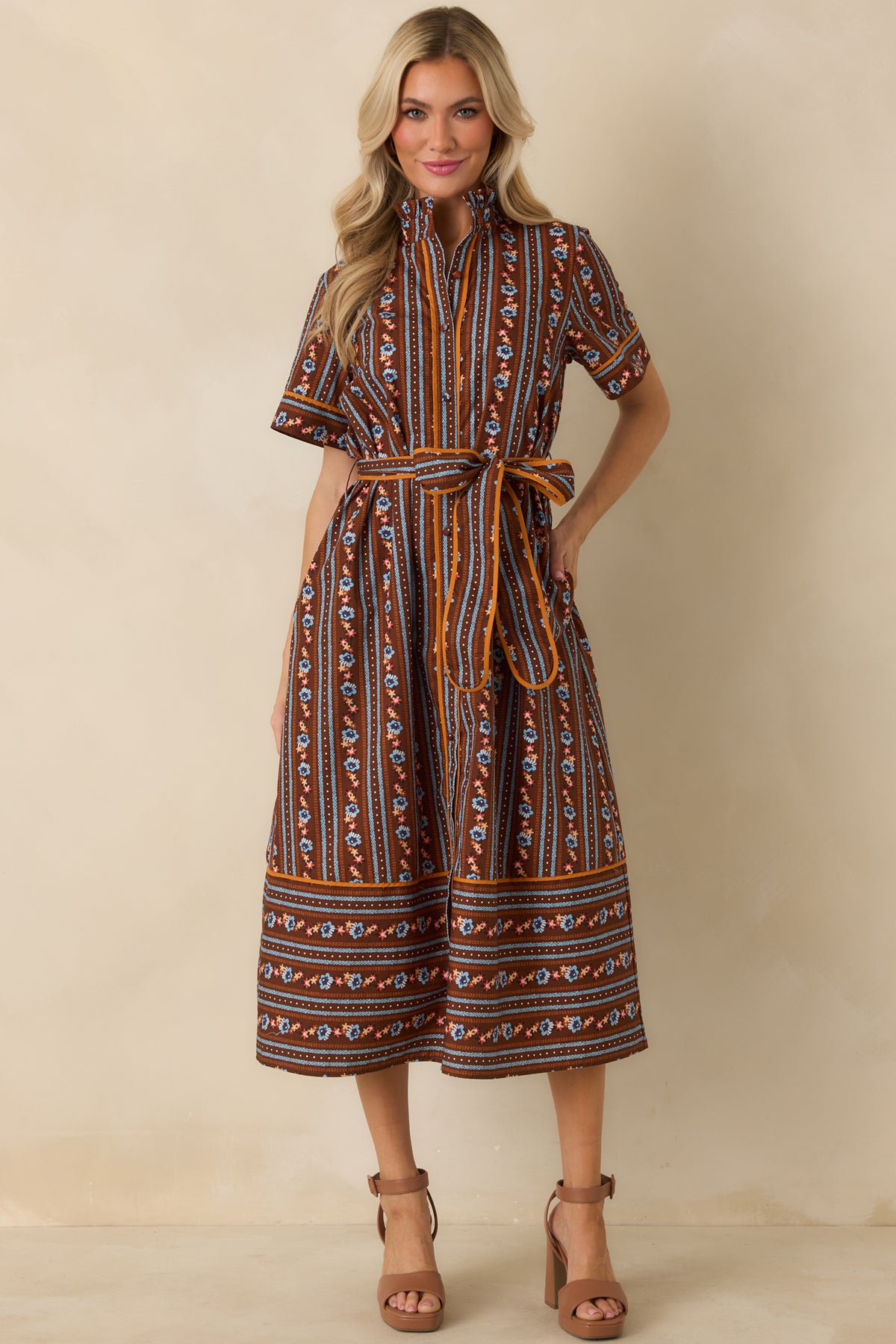 Rich brown A-line dress decorated with blue, orange, ivory, and rust stripes, short sleeves, and a coordinating waist tie.