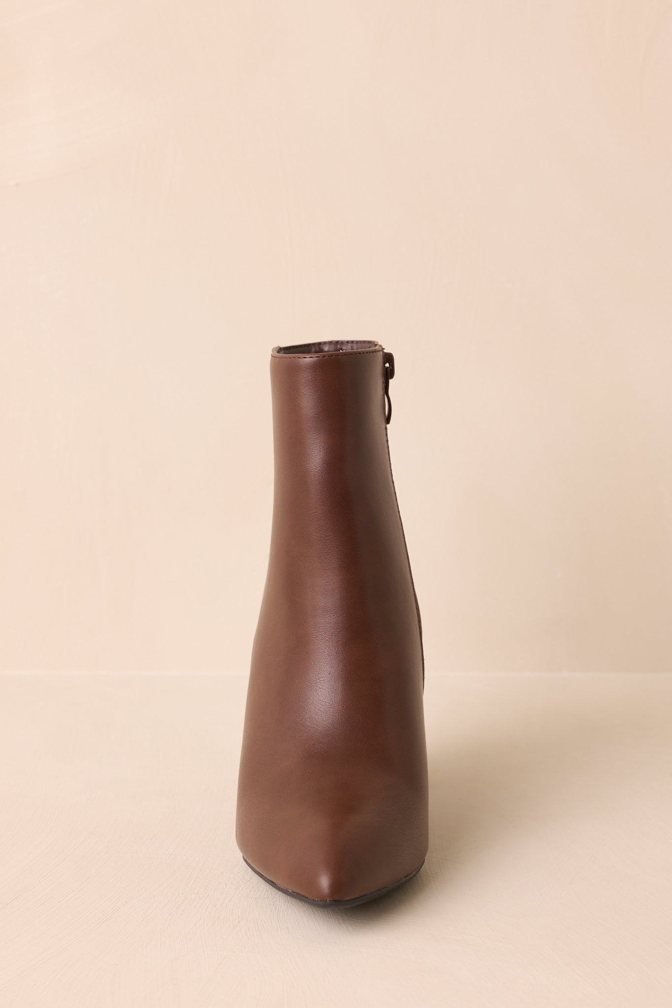 A straight-on front shot of the brown ankle boots capturing the pointed toe and glossy finish.
