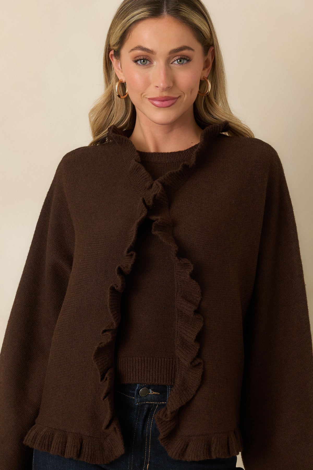 Front view of brown cape-inspired cardigan with an open front, wide long sleeves, and soft ruffle trim.
