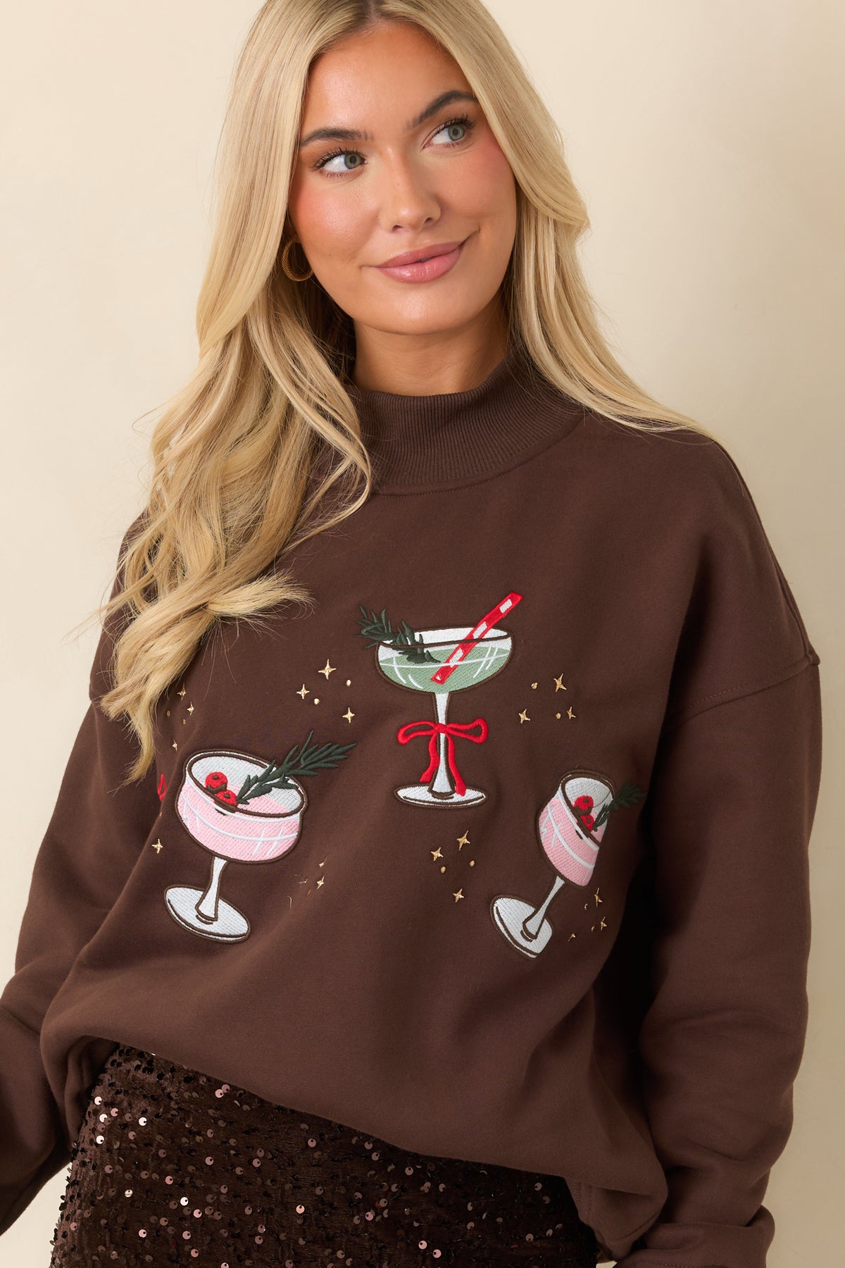 Brown pullover featuring embroidered cocktail glasses, colorful garnishes, and scattered metallic-look star motifs.