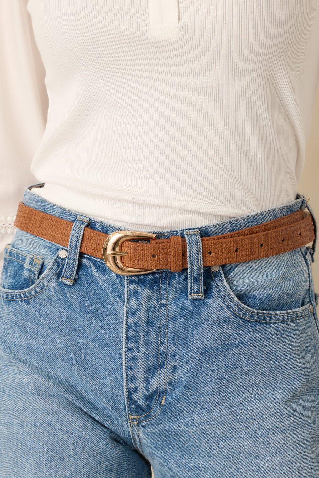 Close-up view of the cognac brown faux leather belt highlighting the woven-texture finish and gold-tone buckle.