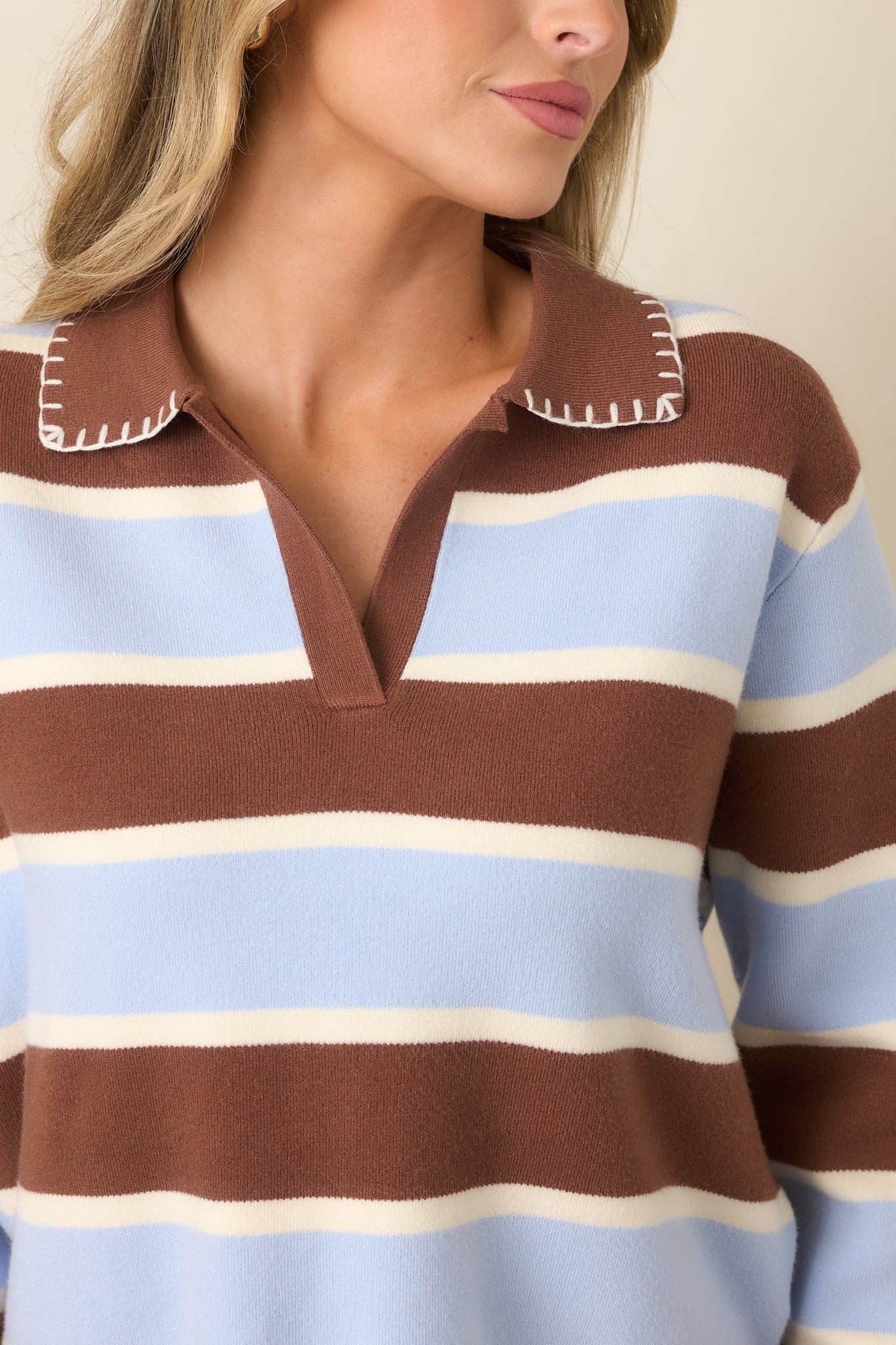 Close-up detail of the knit top highlighting the contrasting brown pointed collar, decorative stitching, V-neckline, and horizontal color-blocked stripes.