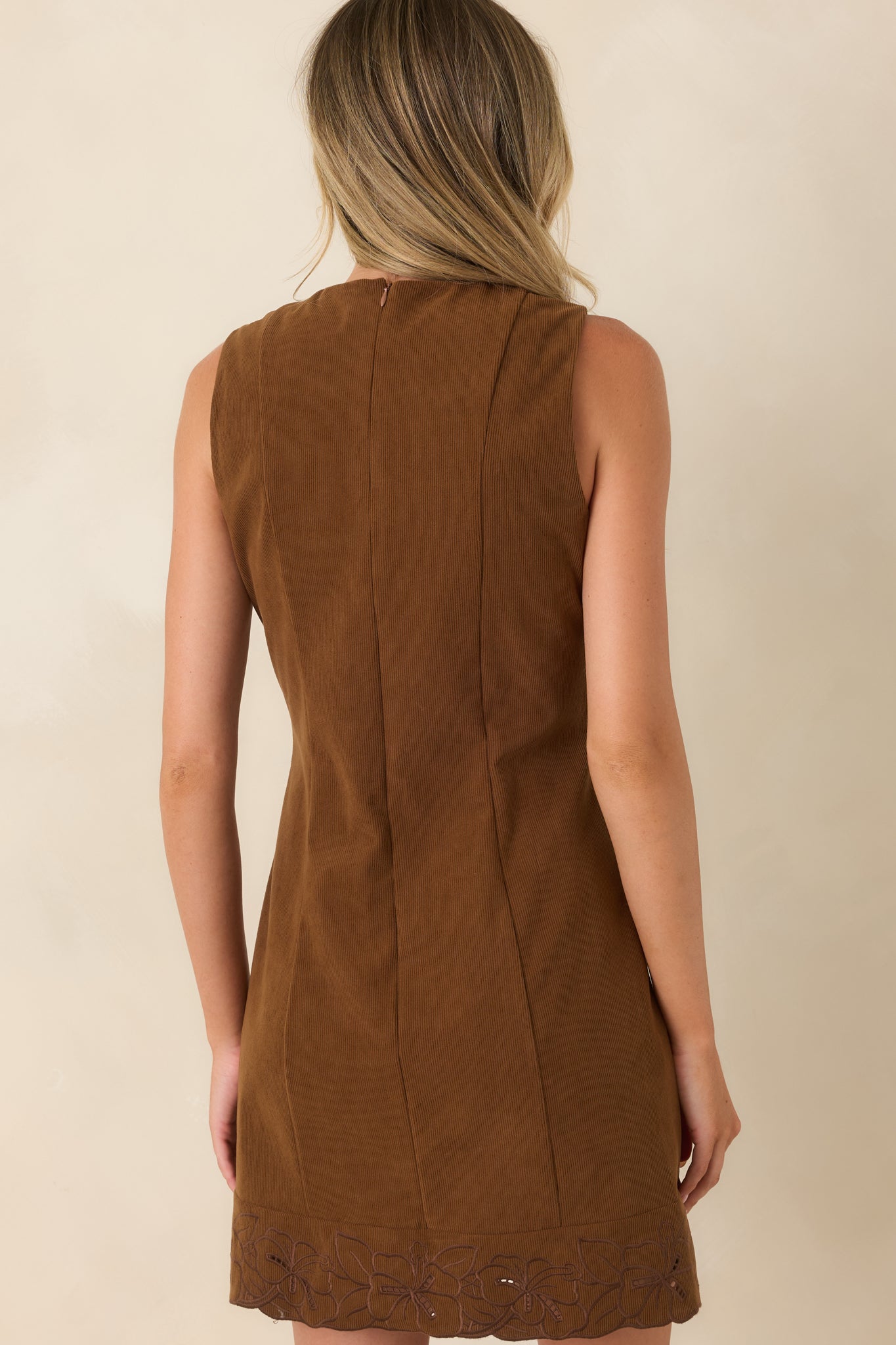 Rear view of the brown corduroy mini dress featuring a concealed back zipper, sleeveless design, vertical seaming, and embroidered scalloped hem.