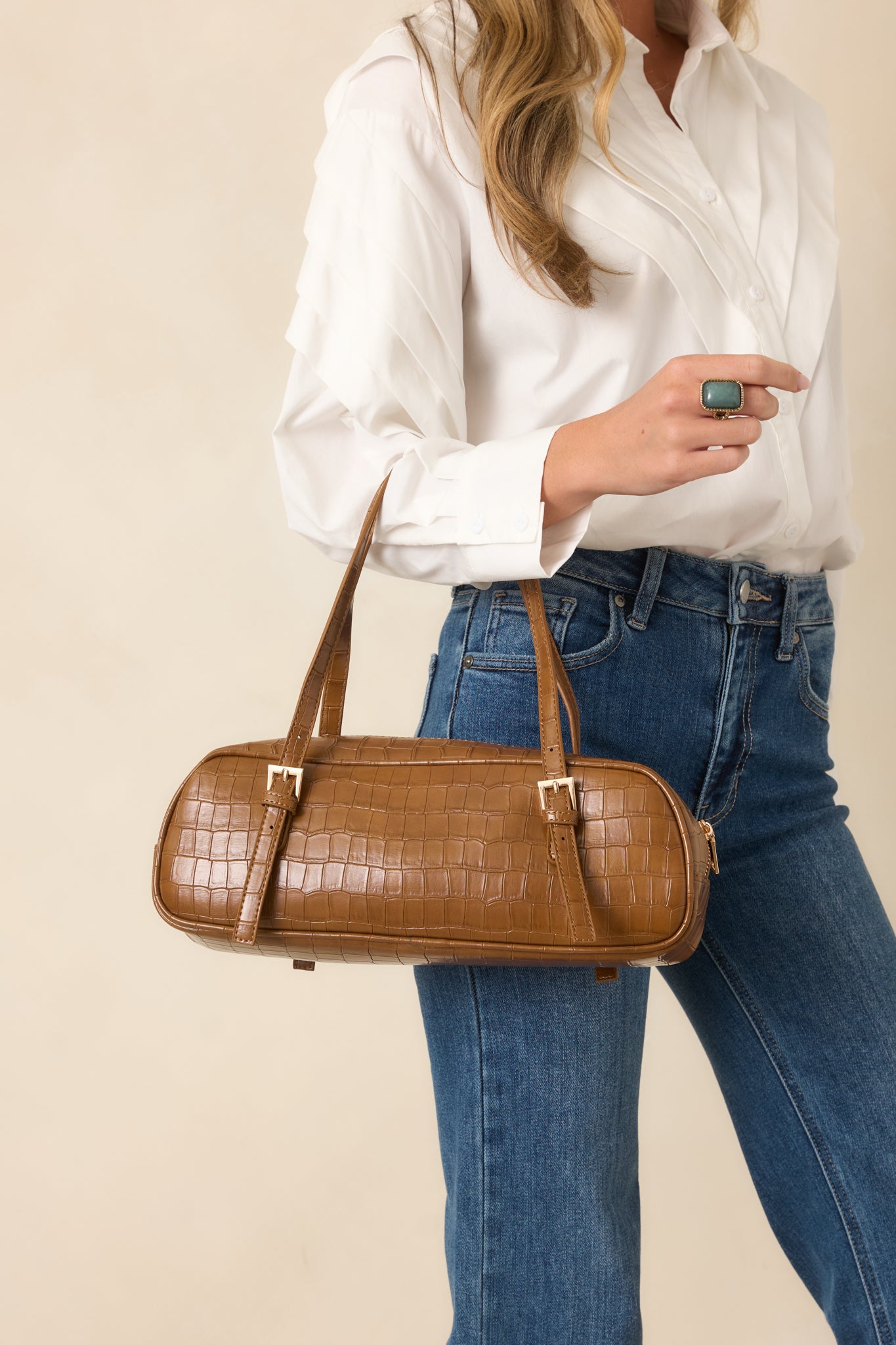 Brown croc-embossed faux leather handbag featuring an elongated shape, structured top handles, zipper closure, and polished texture.