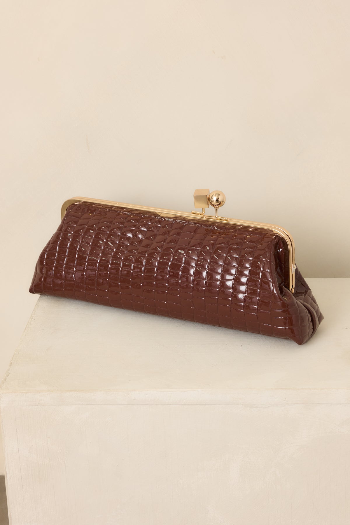 Brown clutch highlighting the raised croc-embossed texture, rectangular shape, and gleaming gold-tone kiss-lock closure.