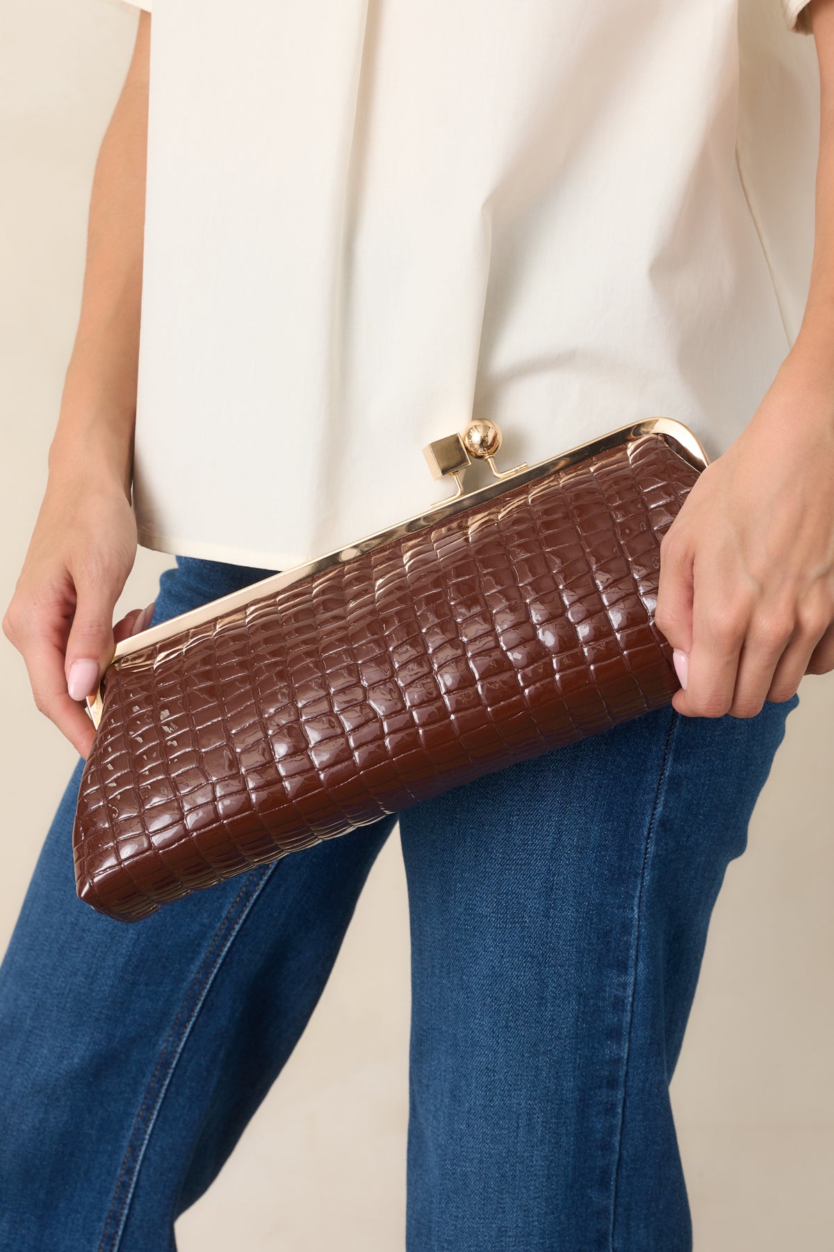Brown rectangular clutch featuring croc-embossed faux leather, a gold-tone kiss-lock frame, and a structured silhouette with optional straps.