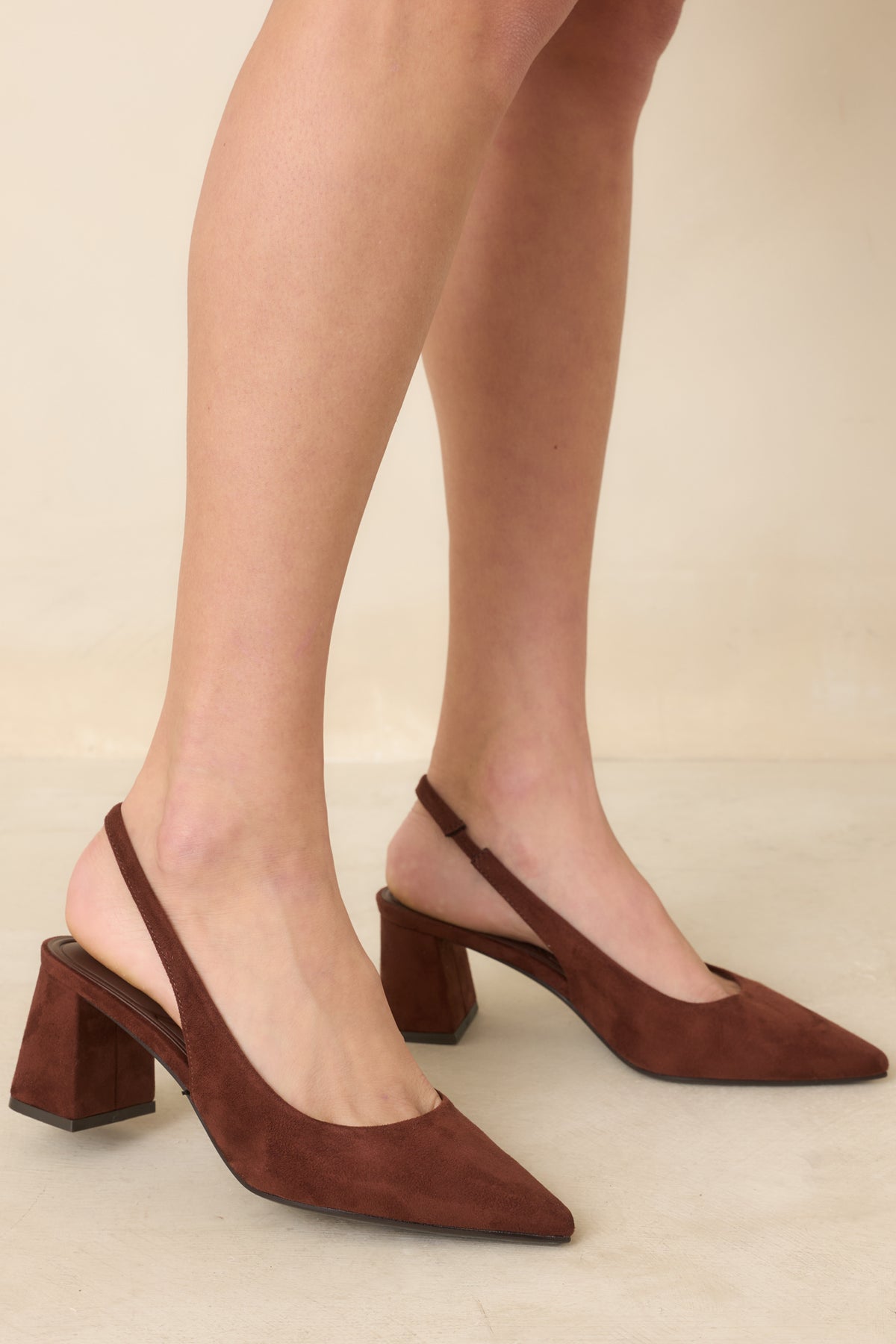 Brown faux suede slingback heels feature pointed toes, slender straps, and covered block heels.