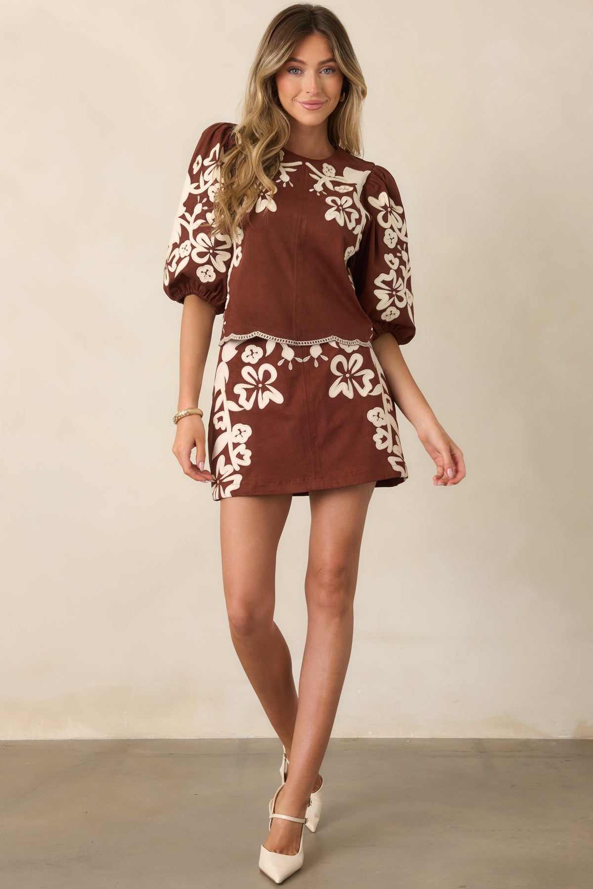 Faux suede mini skirt showcasing winding ivory floral appliqués against a rich brown background.