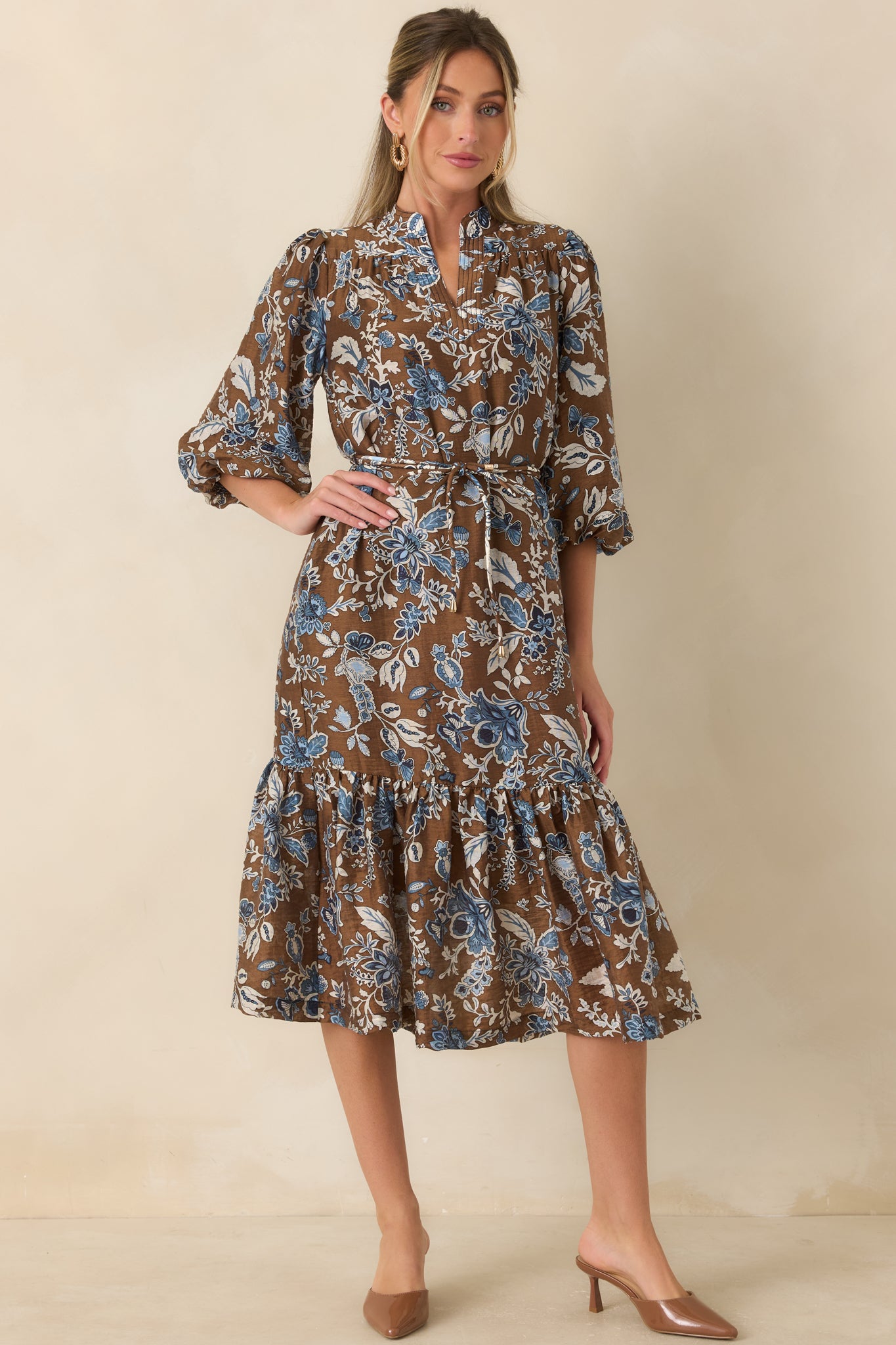 Brown floral print dress featuring a split band collar, gathered waist tie, voluminous sleeves, and ruffle-trimmed midi length.