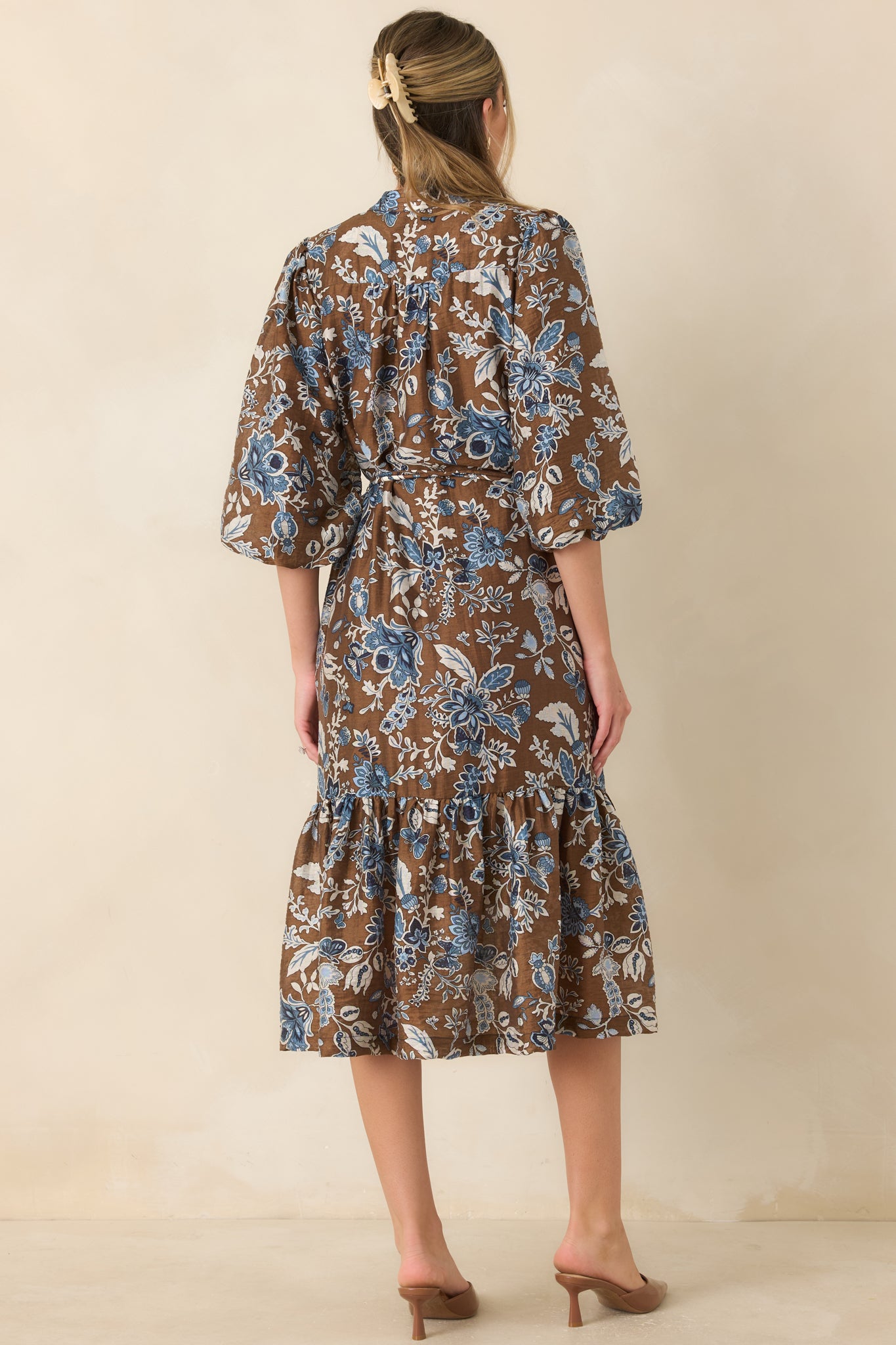 Rear view of the floral midi dress featuring a warm brown print, three-quarter balloon sleeves, removable tie belt, and flowing ruffle hem.