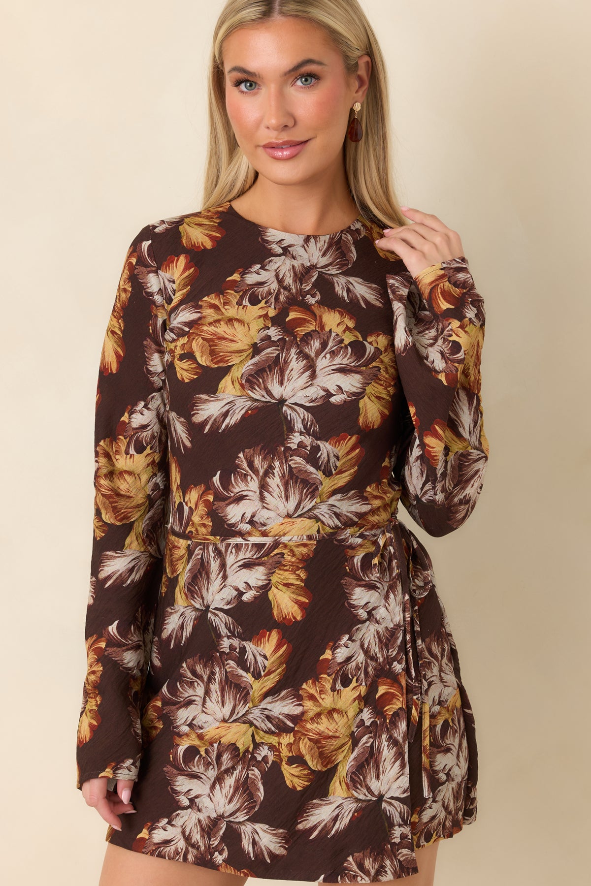 Round neckline and fitted bodice frame the oversized golden yellow and ivory floral print on the brown dress.