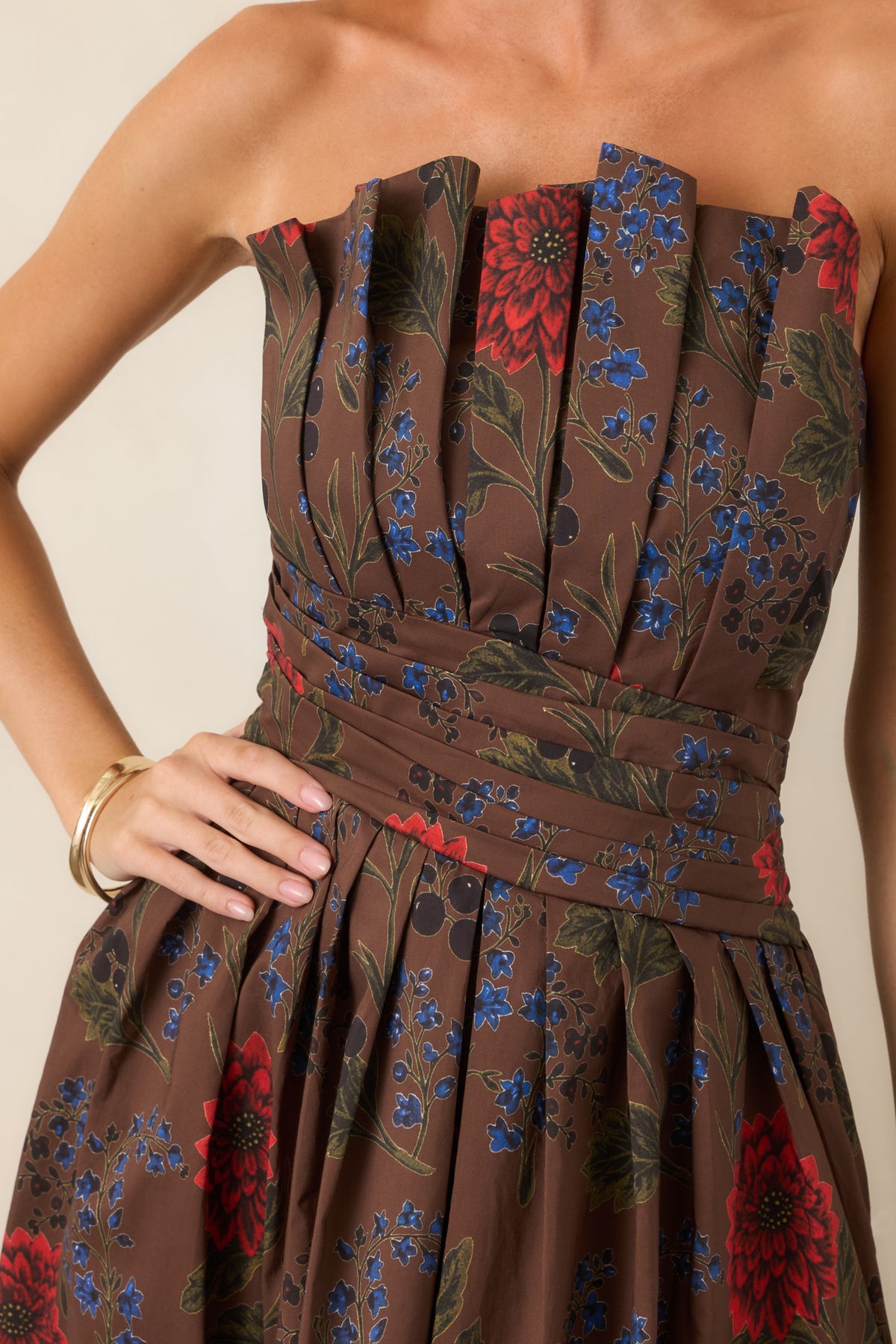 Close-up of a brown floral strapless dress featuring sculptural bodice pleats and layered waist detailing.