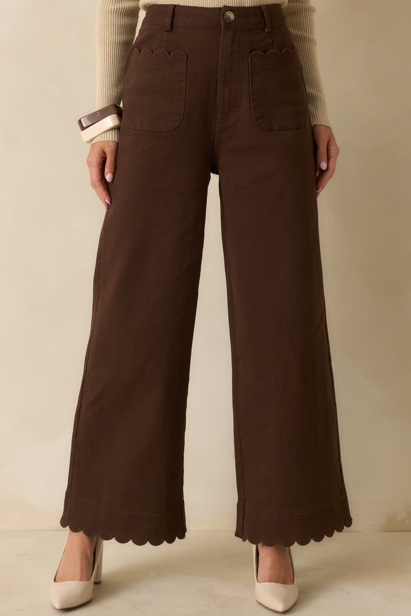 Brown high-waisted wide-leg pants with front patch pockets featuring scalloped trim and structured cotton fabric.