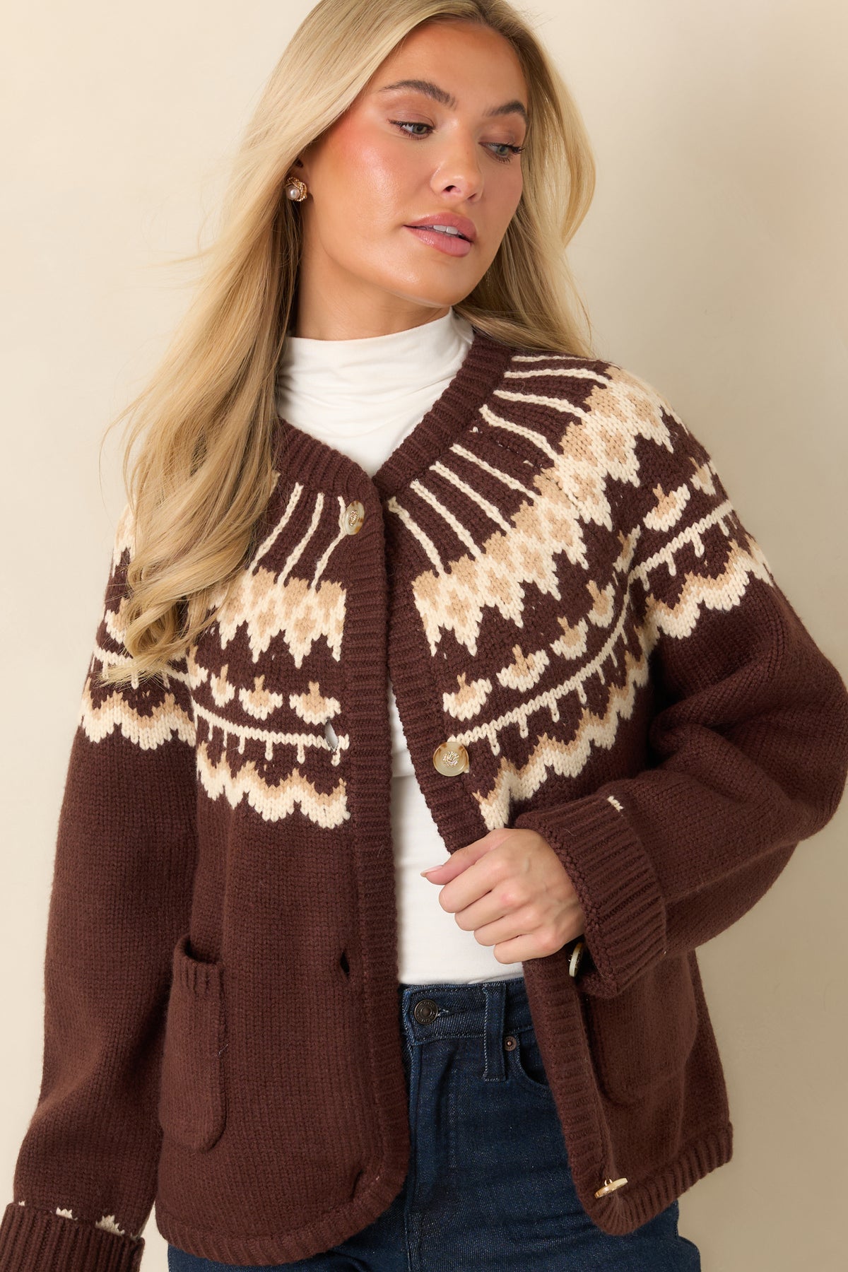 Decorative gold-tone buttons line the front of the brown knit cardigan above two patch pockets.
