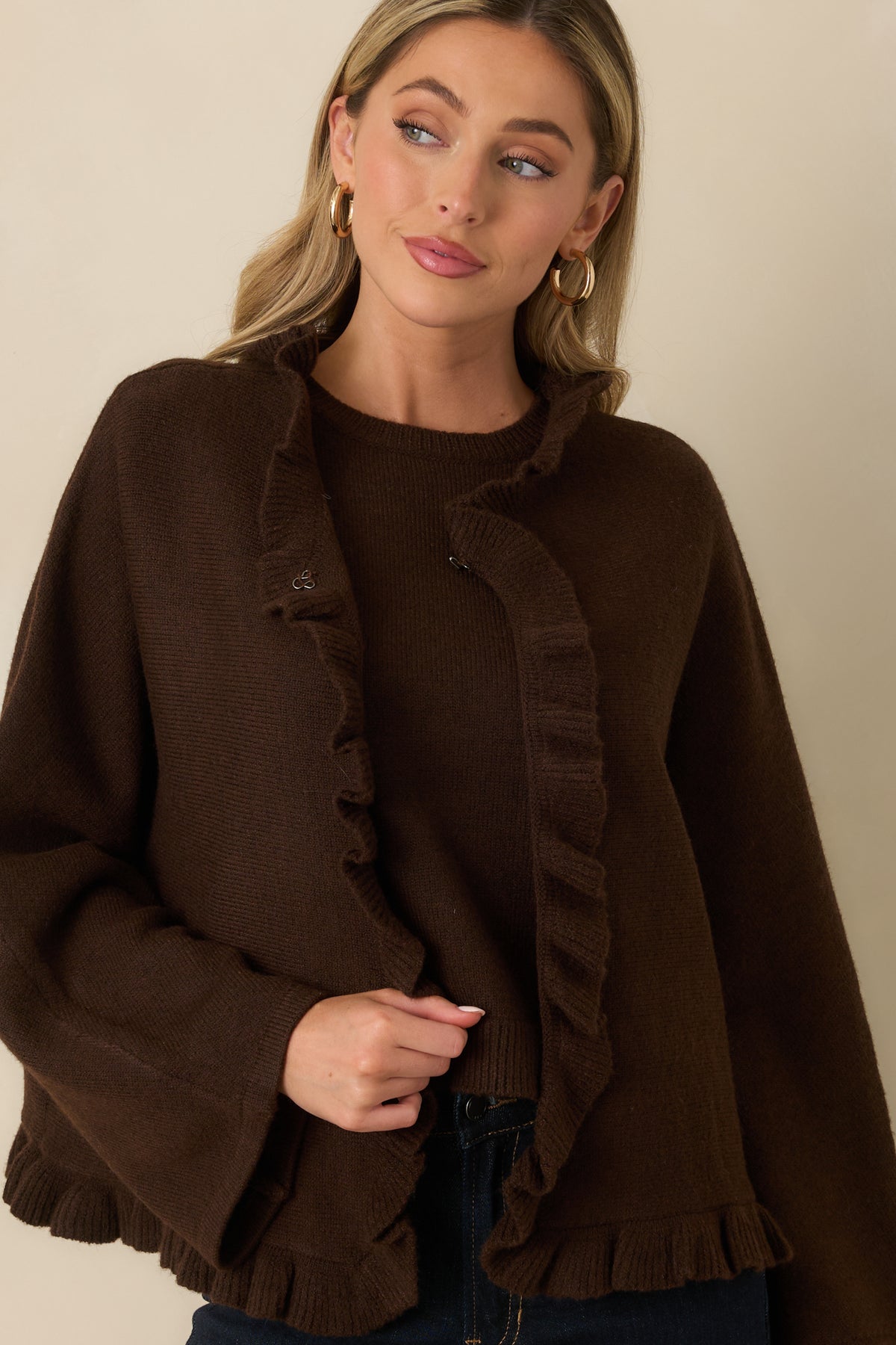 Close-up of brown knit cardigan showing the hook-and-eye closure and textured ruffle trim along the opening.