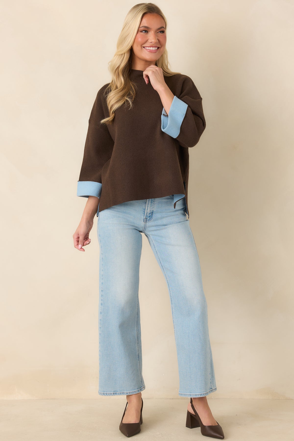Rich brown knit top with a ribbed mock neckline, dropped shoulders, and light blue turnback cuffs.