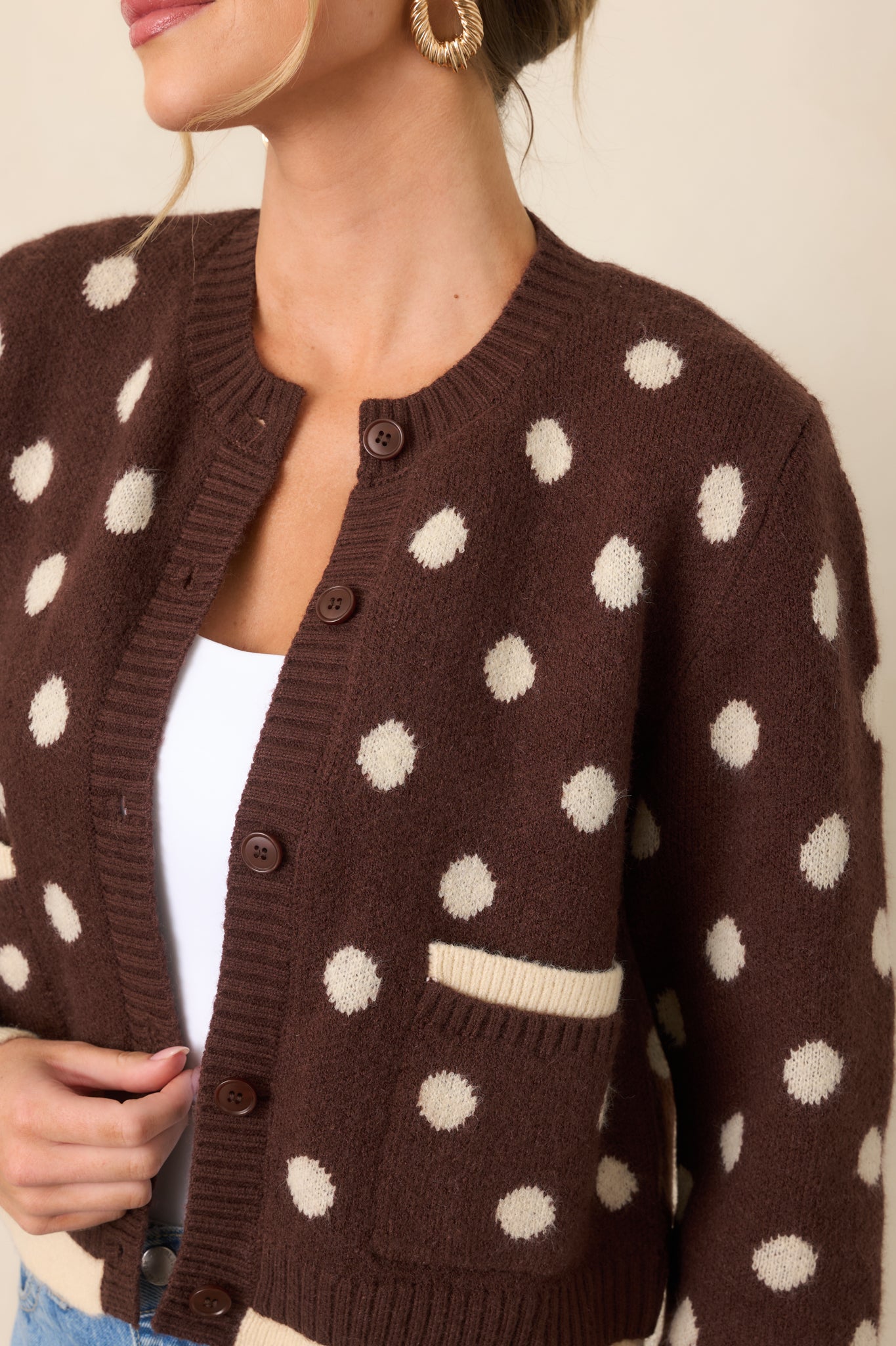 Close-up highlights the soft knit texture, ivory polka dots, front buttons, and contrasting ribbed trim.